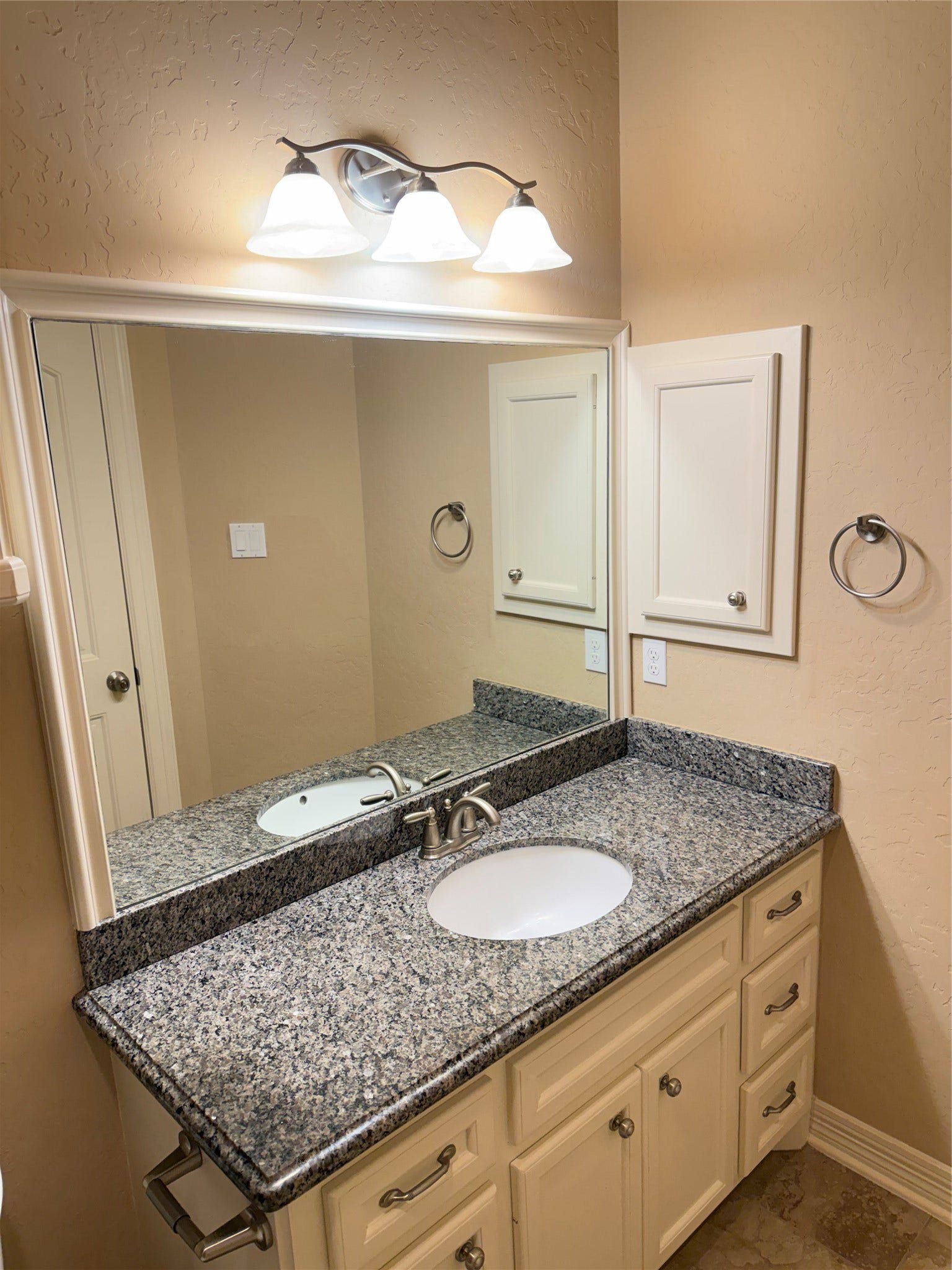 19841 S Plantation Estates Drive, Porter, TX 77365 Elegant bathroom featuring a sleek granite countertop, undermount sink, and ample cabinet storage, complemented by a large mirror and modern lighting.