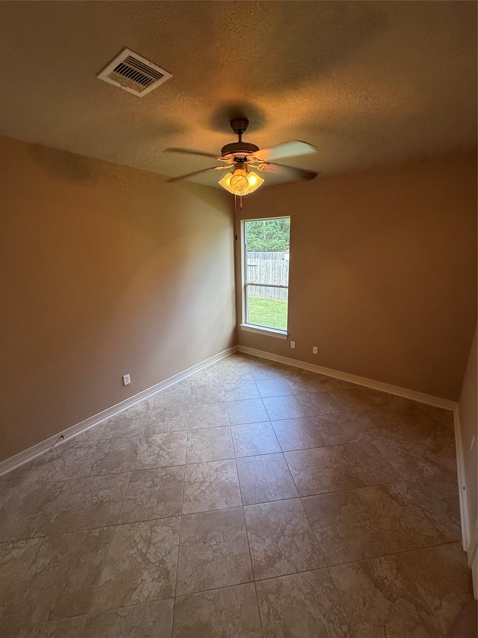 19841 S Plantation Estates Drive, Porter, TX 77365 Cozy room with elegant tile flooring, warm walls, and a ceiling fan, featuring a window that overlooks a private fenced backyard.