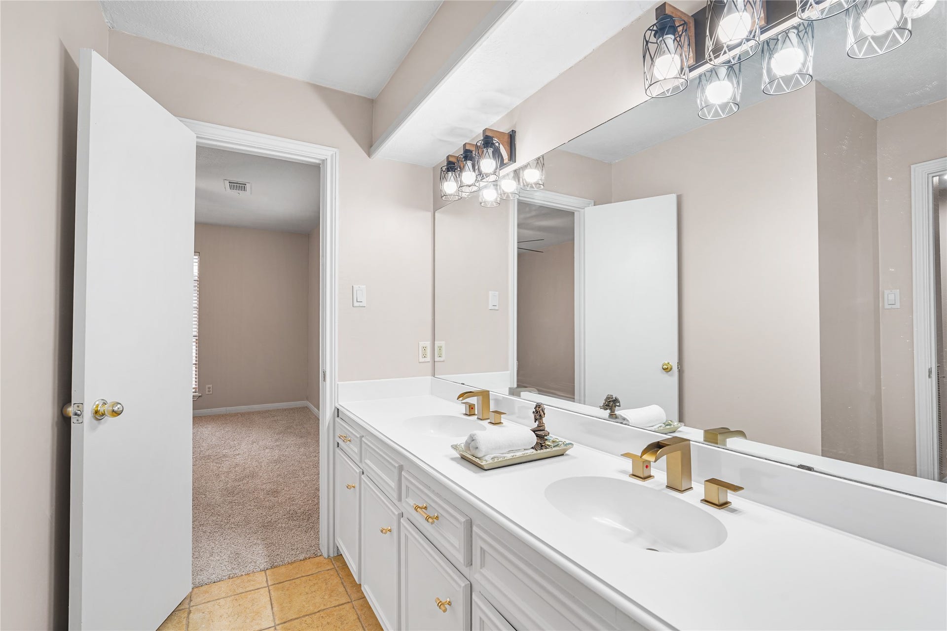 Bright bathroom featuring a double vanity with sleek gold fixtures, ample counter space, and modern lighting.