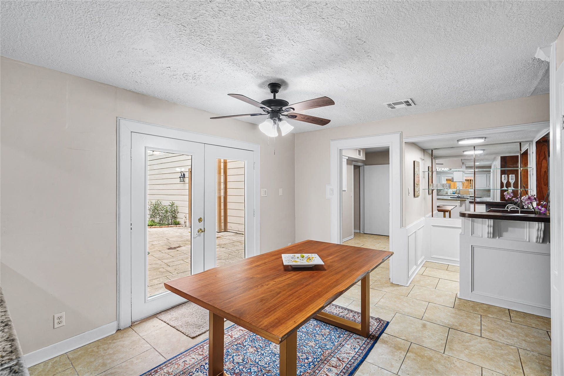 Bright dining area with French doors opening to backyard, tiled flooring, and a ceiling fan for added comfort.