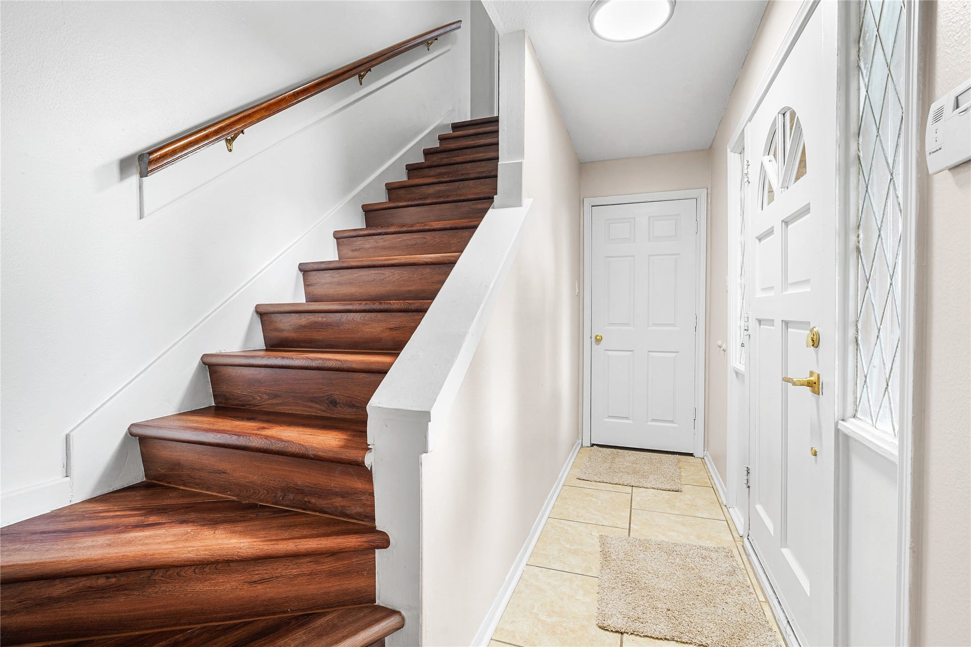 Inviting secondary entryway featuring rich hardwood stairs, a bright white door, and tiled flooring, offering a warm welcome into the home.