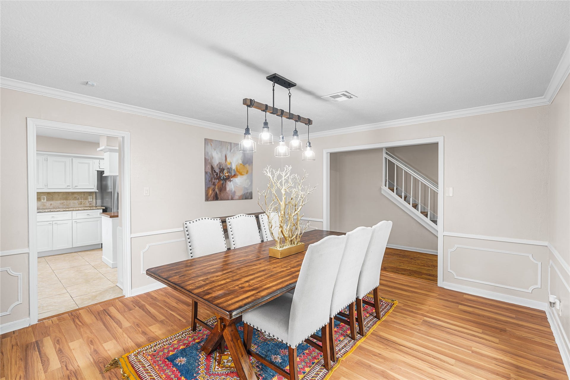 Elegant dining room with hardwood floors and stylish pendant lighting. The space opens to a bright kitchen.