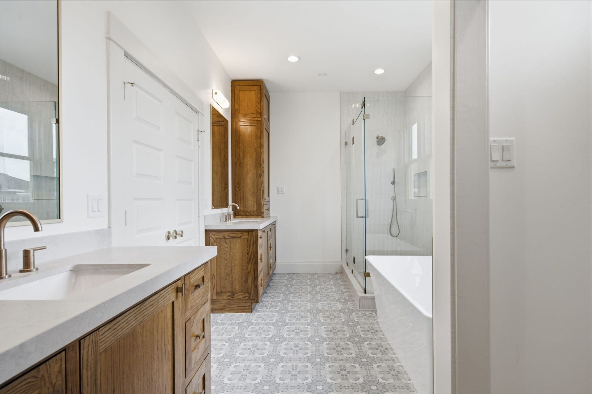 404 Avondale Street, Houston, TX 77006 Spacious bathroom featuring elegant wood cabinetry, dual sinks, and a sleek glass-enclosed shower, complemented by stylish patterned floor tiles for a modern touch.