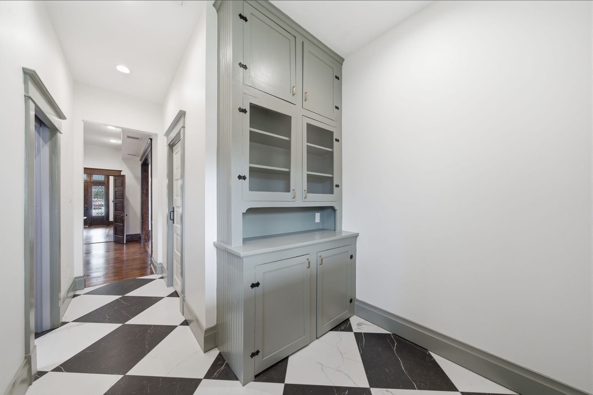 404 Avondale Street, Houston, TX 77006 Spacious hallway featuring elegant black and white checkered flooring and ORIGINAL built-in cabinetry, leading to a warmly lit room with rich wooden floors.