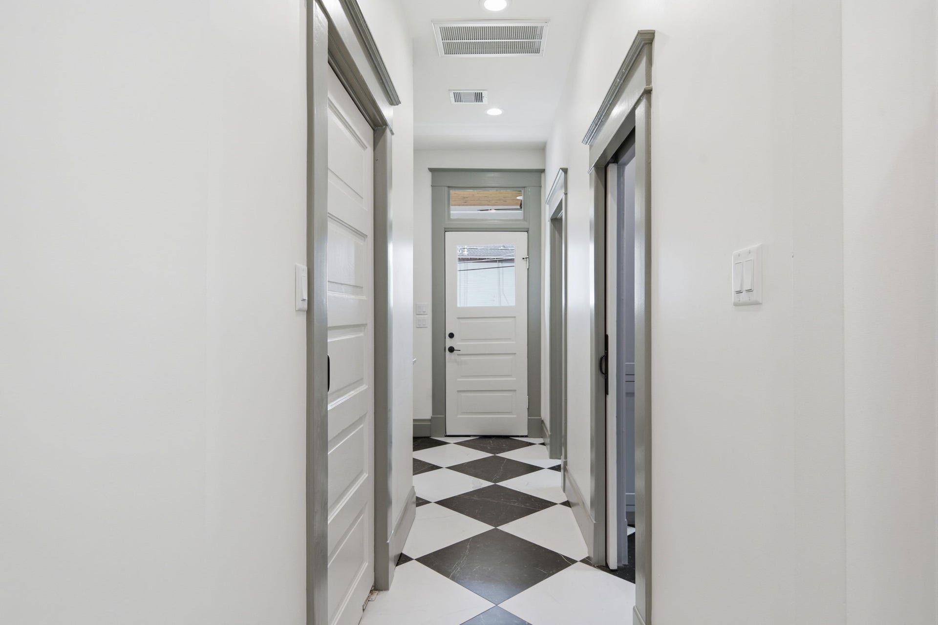 404 Avondale Street, Houston, TX 77006 Bright hallway with modern black and white checkered flooring, leading to multiple rooms and a back door, offering a clean and inviting space.