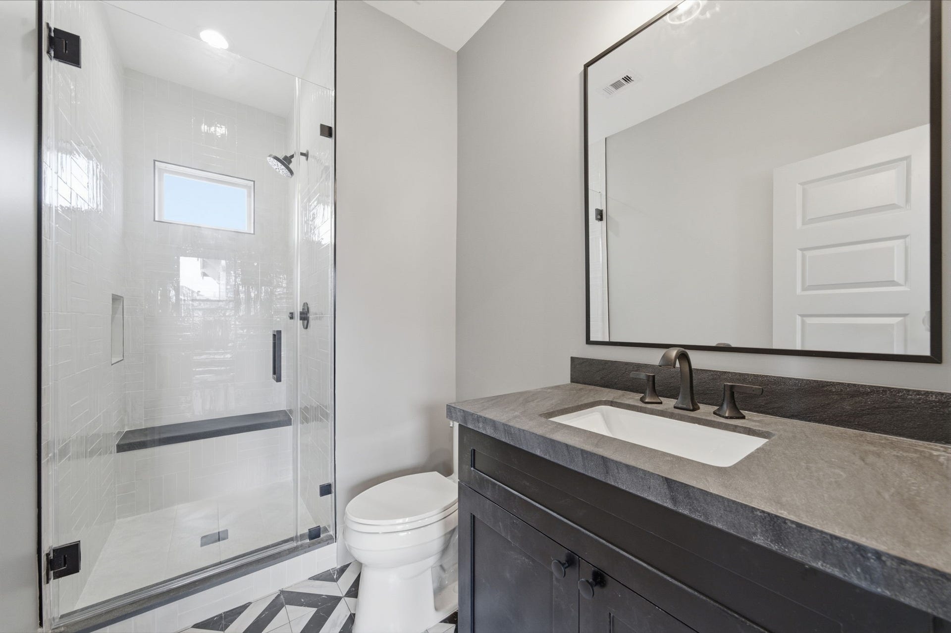 404 Avondale Street, Houston, TX 77006 Modern bathroom featuring a sleek glass-enclosed shower with a built-in bench, stylish geometric tile flooring, and a sophisticated dark vanity with a large mirror.