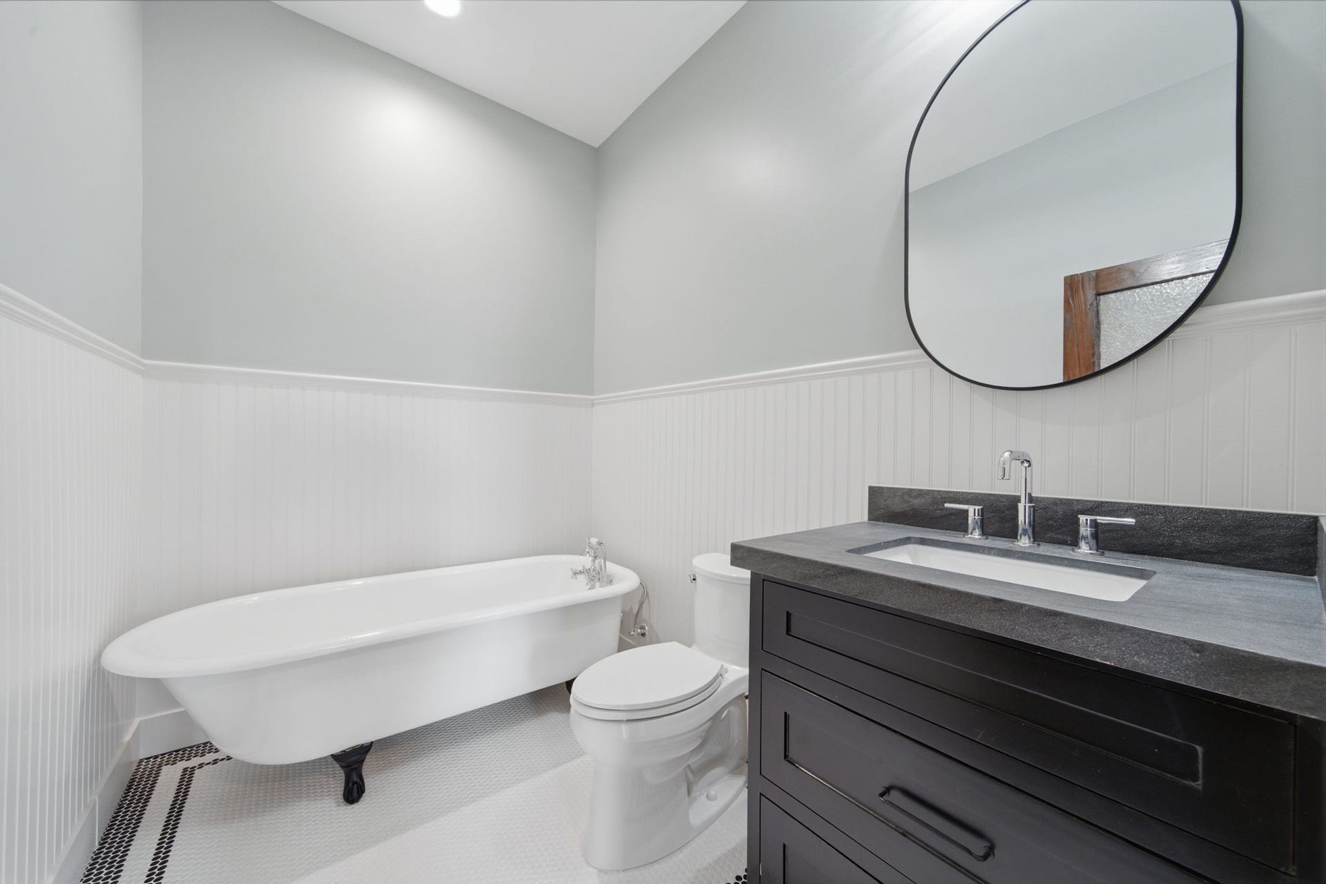 404 Avondale Street, Houston, TX 77006 Elegant bathroom featuring a classic clawfoot tub, sleek black vanity with modern fixtures, and a stylish oval mirror, all accented by crisp white wainscoting.