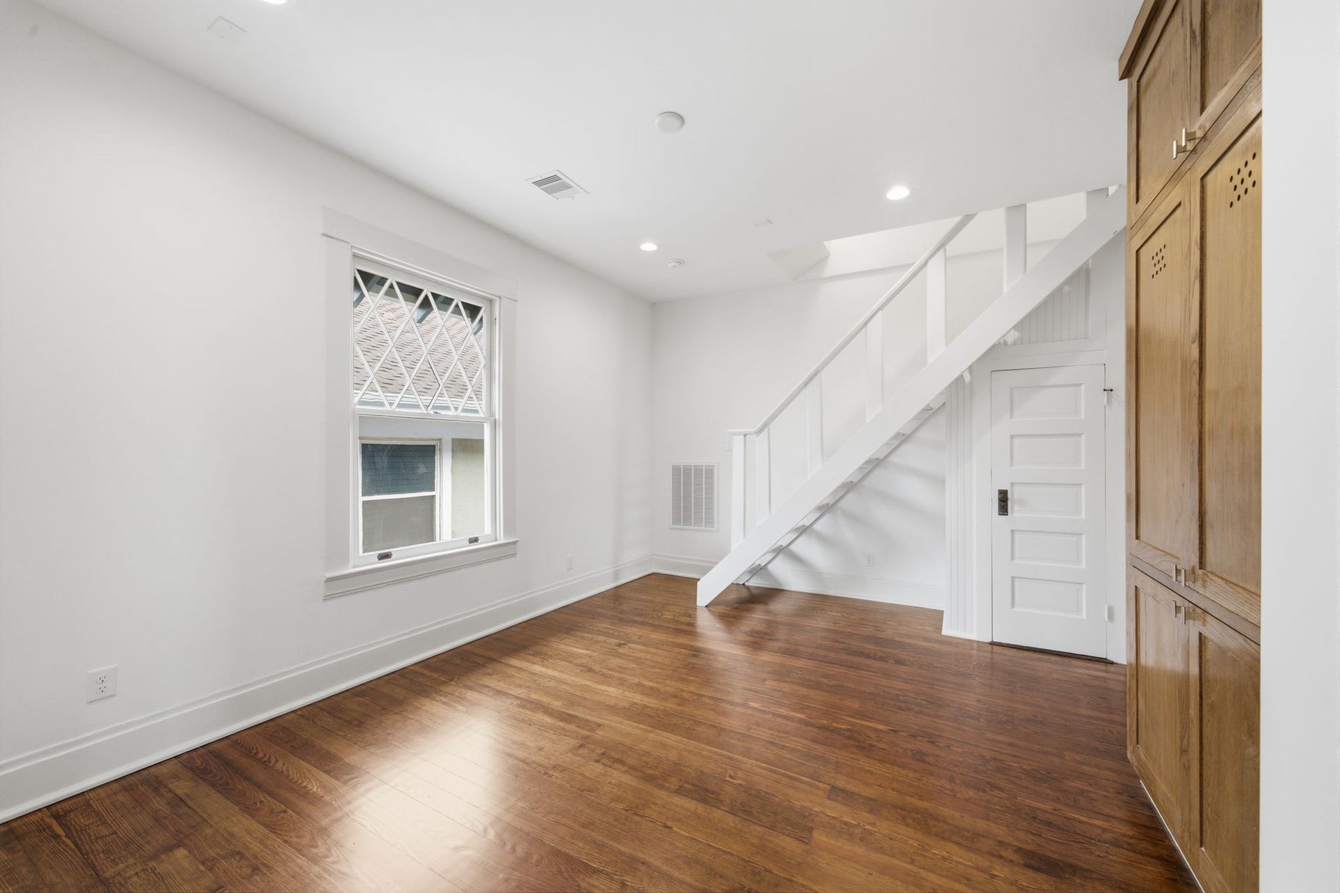 404 Avondale Street, Houston, TX 77006 Charming room featuring rich hardwood floors, a stylish staircase to the 3rd story, ample natural light from a large window, and warm wooden cabinetry for storage.