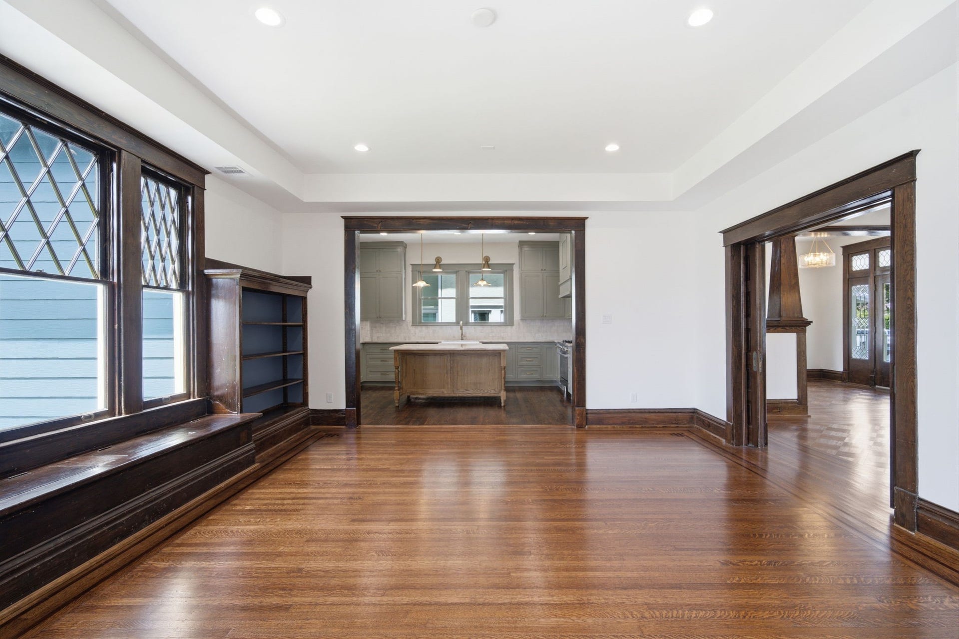 404 Avondale Street, Houston, TX 77006 Elegant living space with rich wood flooring and trim, featuring built-in shelving and large windows. The open layout seamlessly connects to a modern kitchen with a central island and stylish cabinetry.