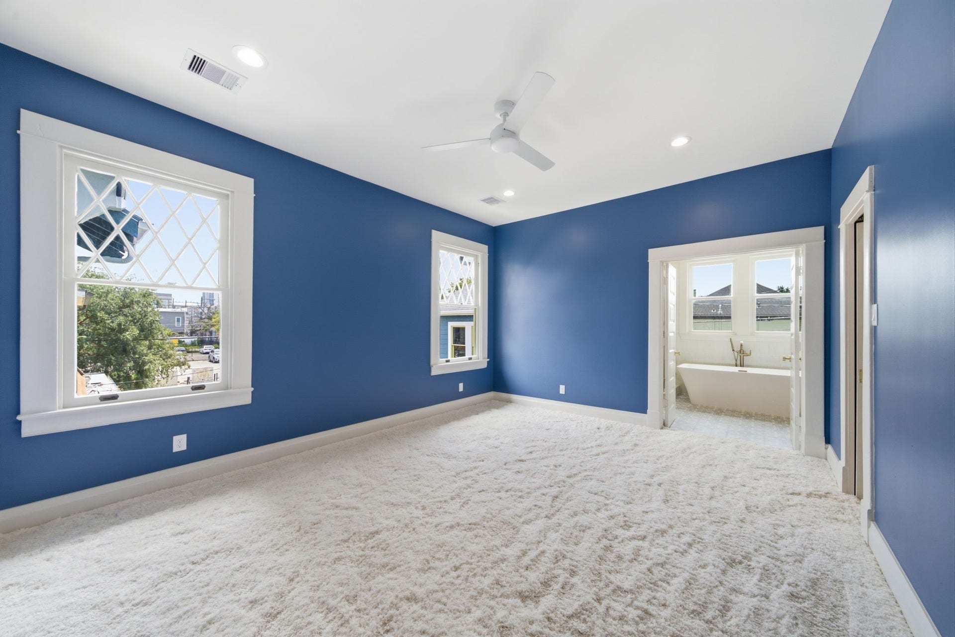 404 Avondale Street, Houston, TX 77006 The primary bedroom with vibrant blue walls, plush carpet, and ample natural light, leading to a luxurious ensuite bathroom with a freestanding tub.