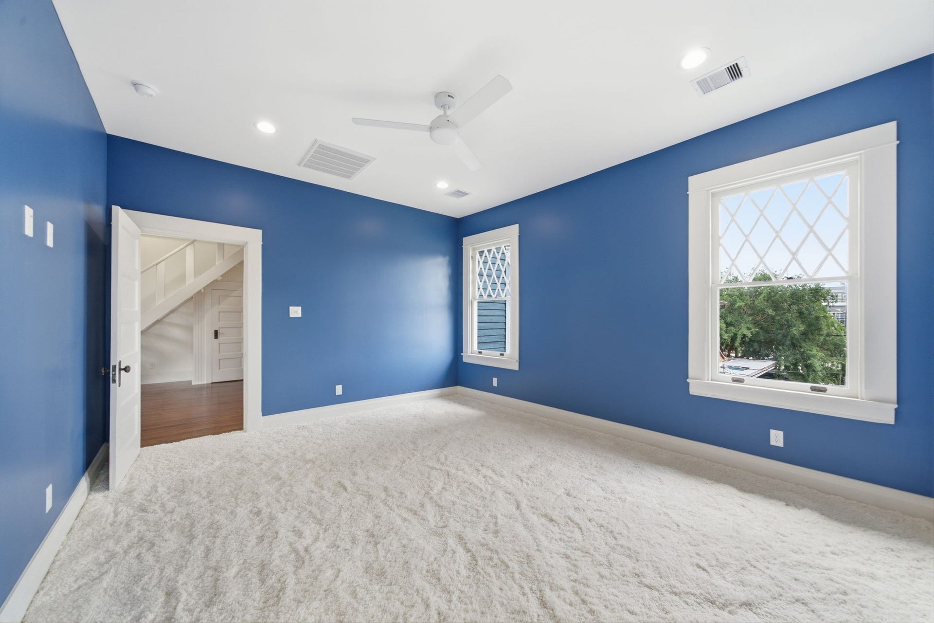 404 Avondale Street, Houston, TX 77006 Spacious bedroom featuring vibrant blue walls, plush carpeting, and ample natural light from large windows, offering a cozy and inviting atmosphere.