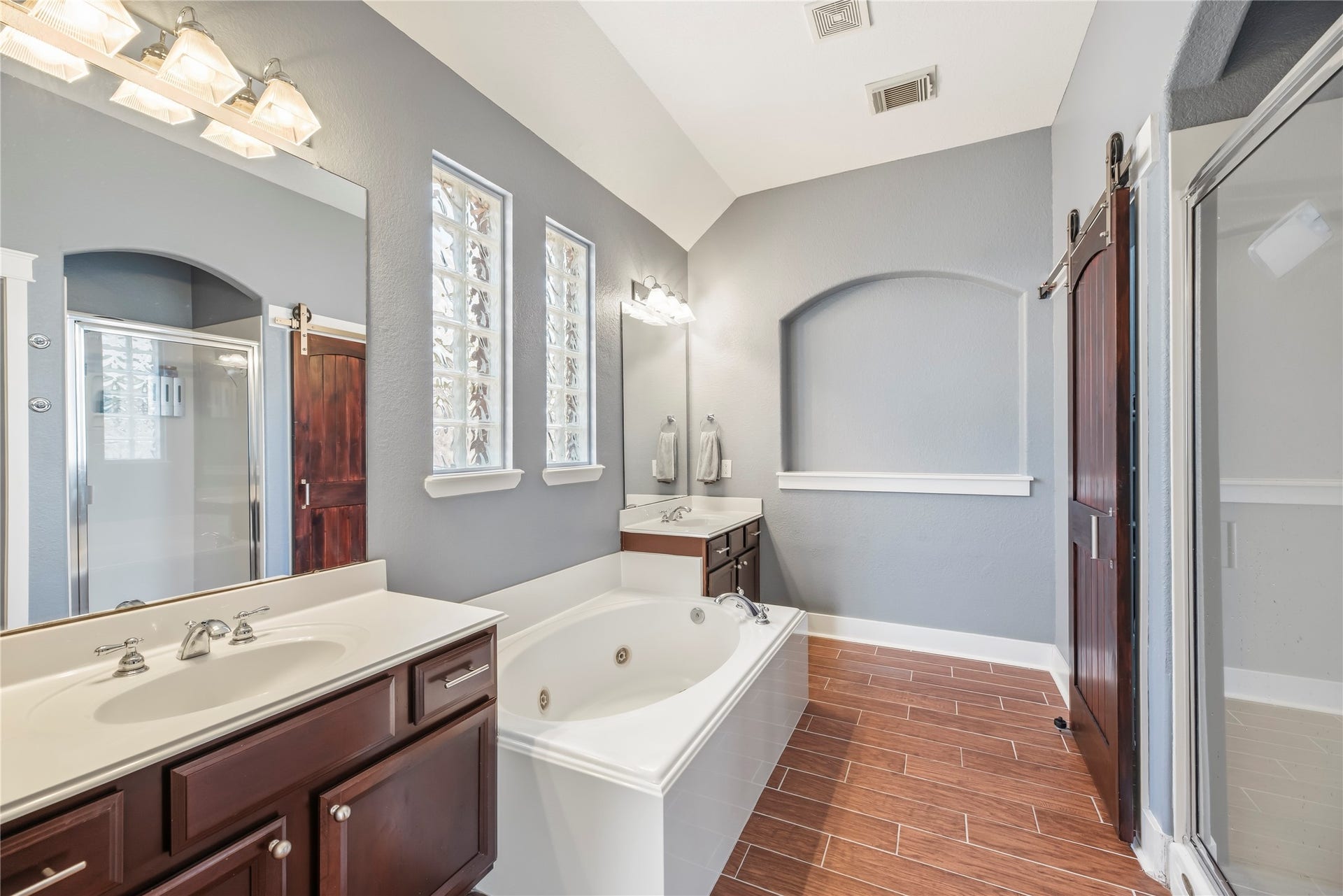 20918 Field Manor Lane, Katy, TX 77450 Elegant bathroom featuring a luxurious soaking tub, dual sinks with rich wood cabinetry, and a spacious glass-enclosed shower and stylish accent windows enhance the space.