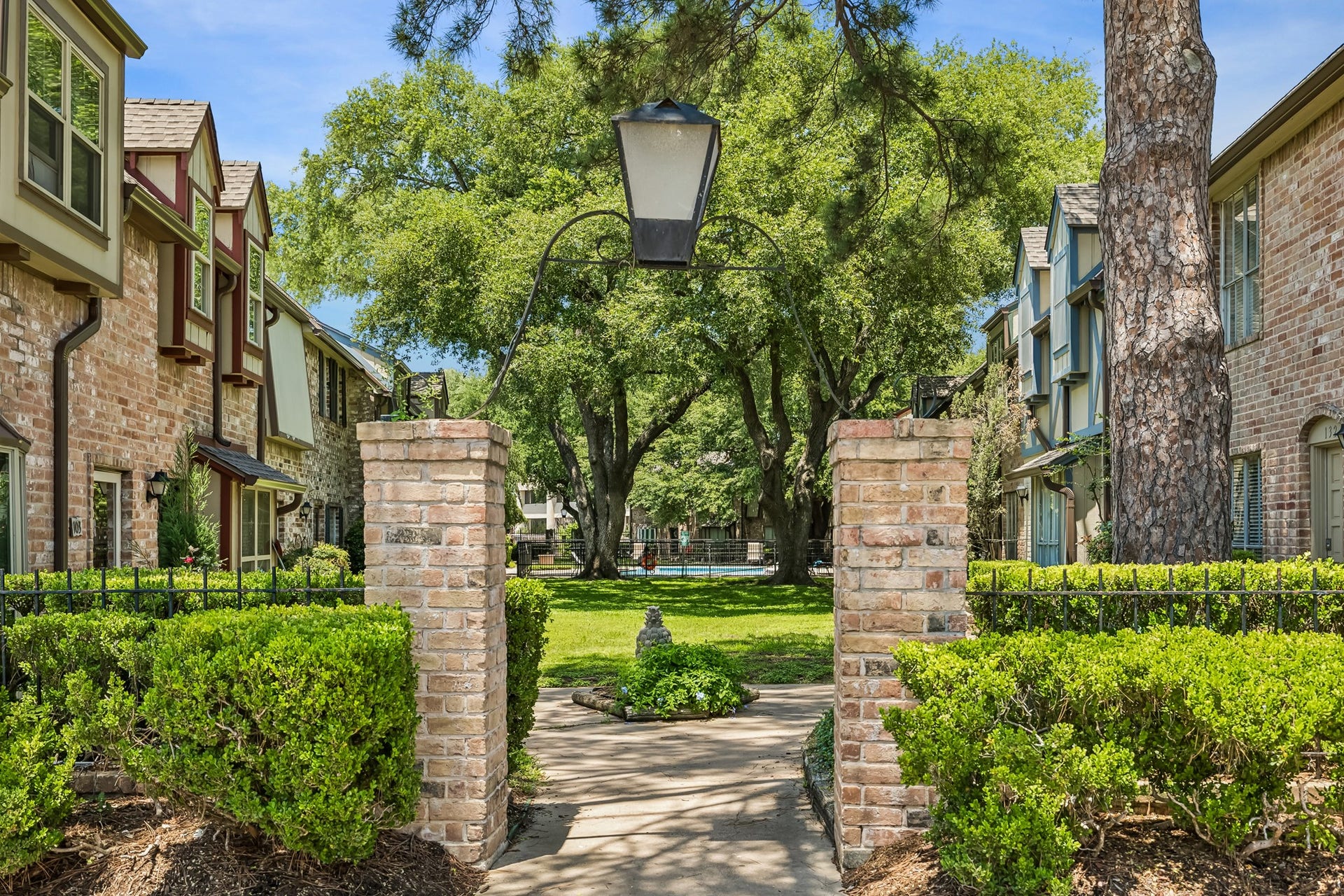 14719 Barryknoll Lane, #51, Houston, TX 77079 A landscaped courtyard with mature trees and brick entry columns creates a welcoming community setting. Shaded walkways and manicured green space connect the townhomes to shared amenities nearby.