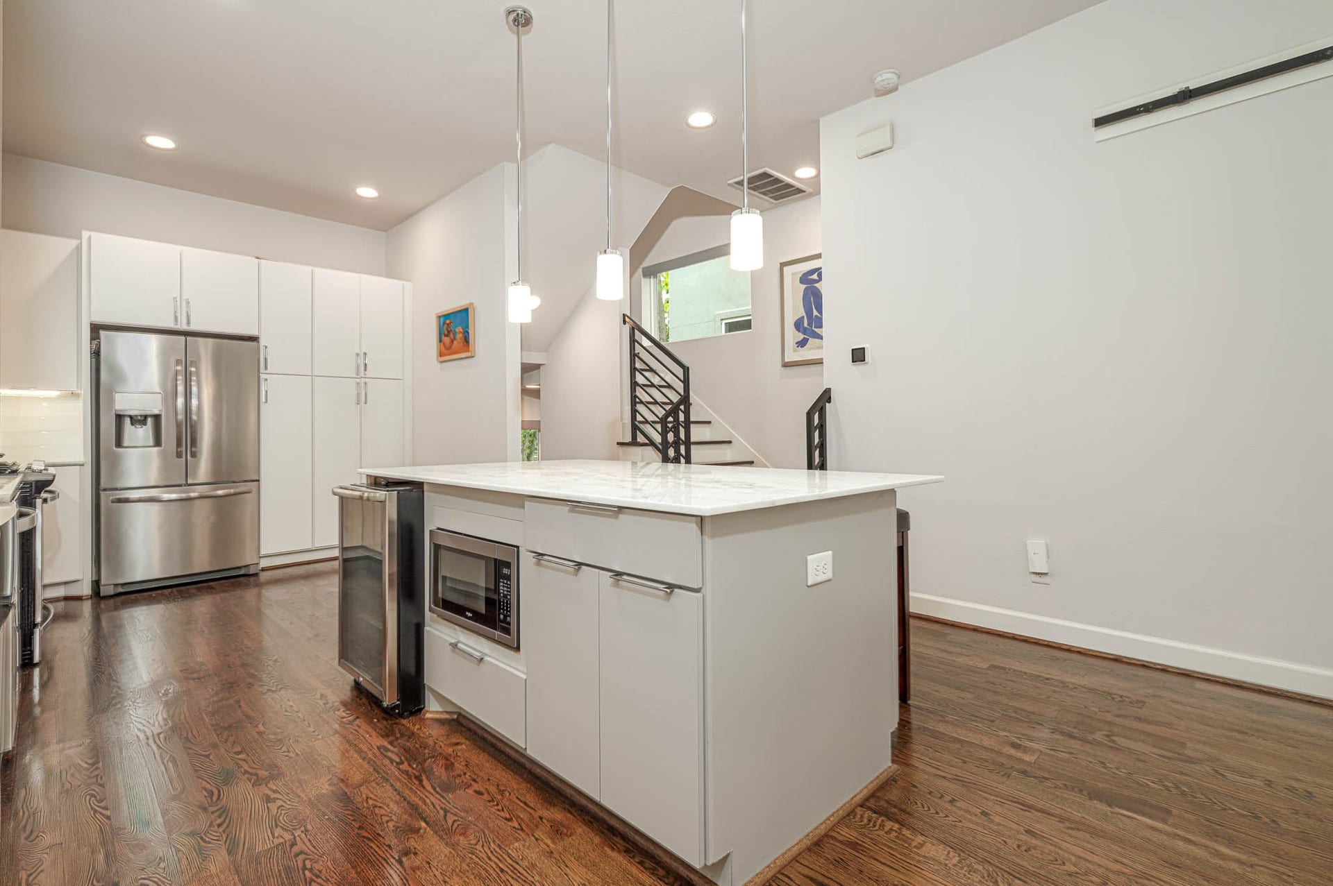 1615 Bingham Street, Houston, TX 77007 Modern kitchen featuring sleek stainless steel appliances, a spacious island with built-in microwave, and elegant hardwood floors, all accented by stylish pendant lighting.