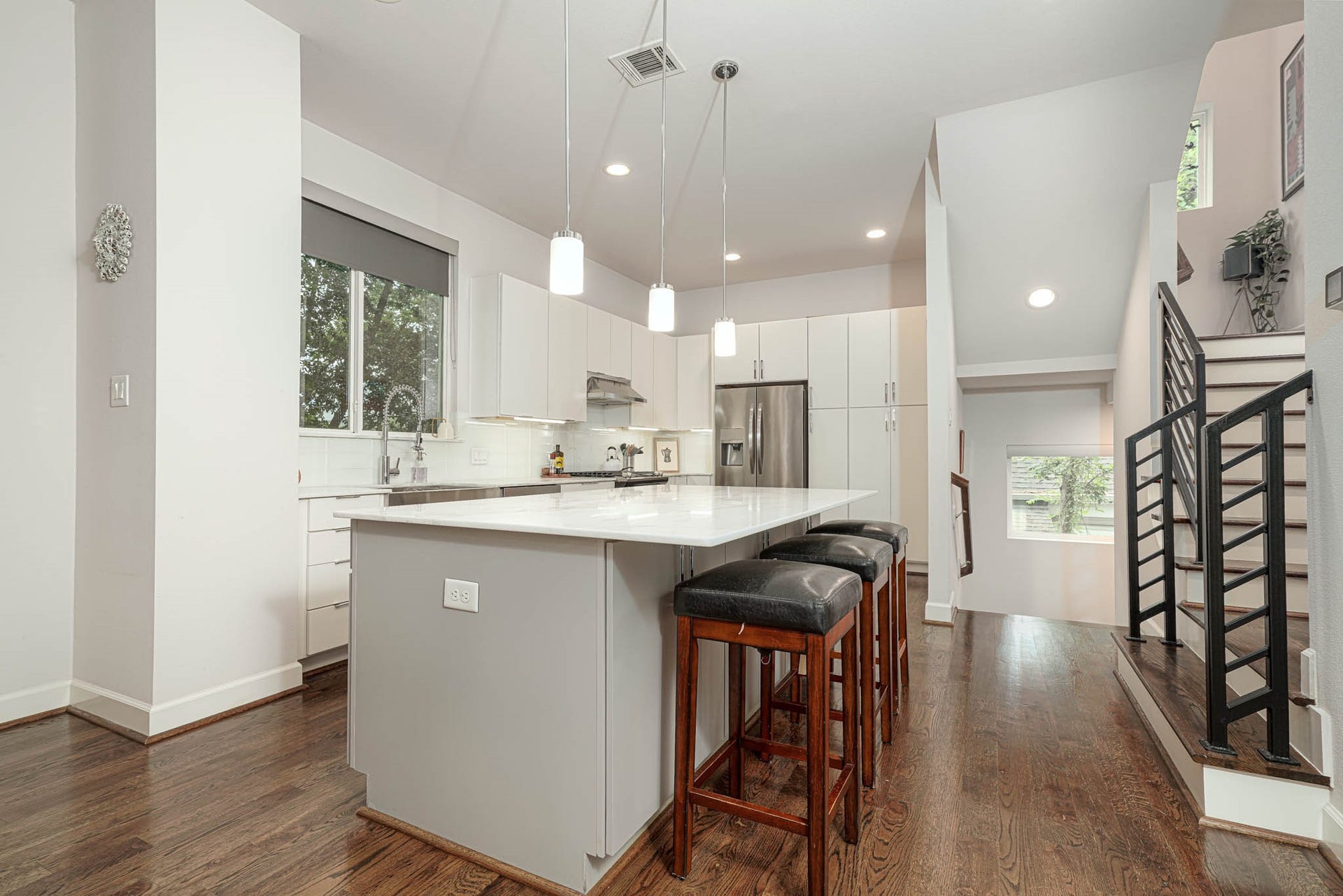 1615 Bingham Street, Houston, TX 77007 Modern kitchen with sleek white cabinetry, stainless steel appliances, and a large island with bar seating, complemented by warm hardwood floors and recessed lighting.