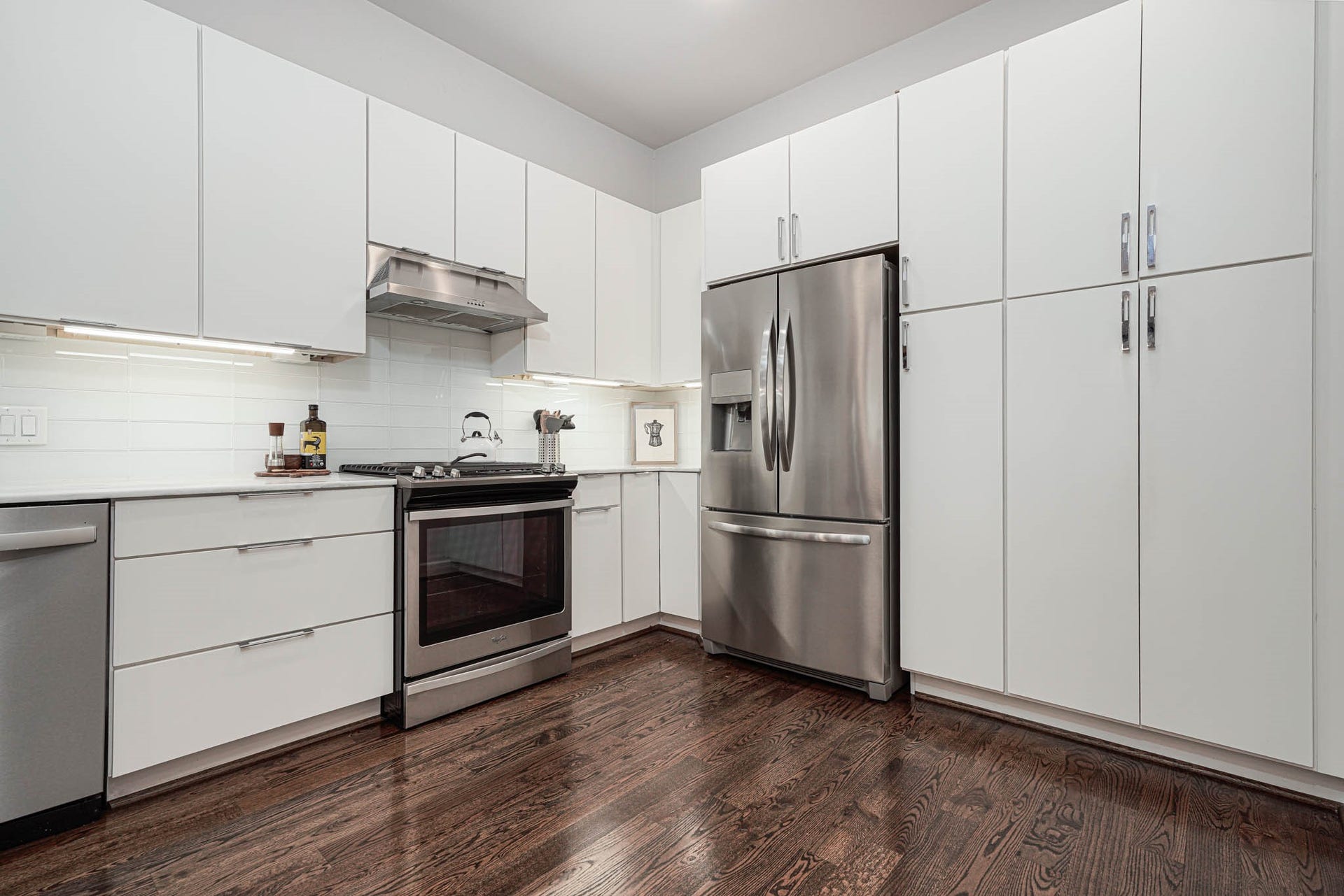 1615 Bingham Street, Houston, TX 77007 A modern kitchen features sleek white cabinetry, stainless steel appliances, and rich hardwood floors, creating a stylish and functional space.