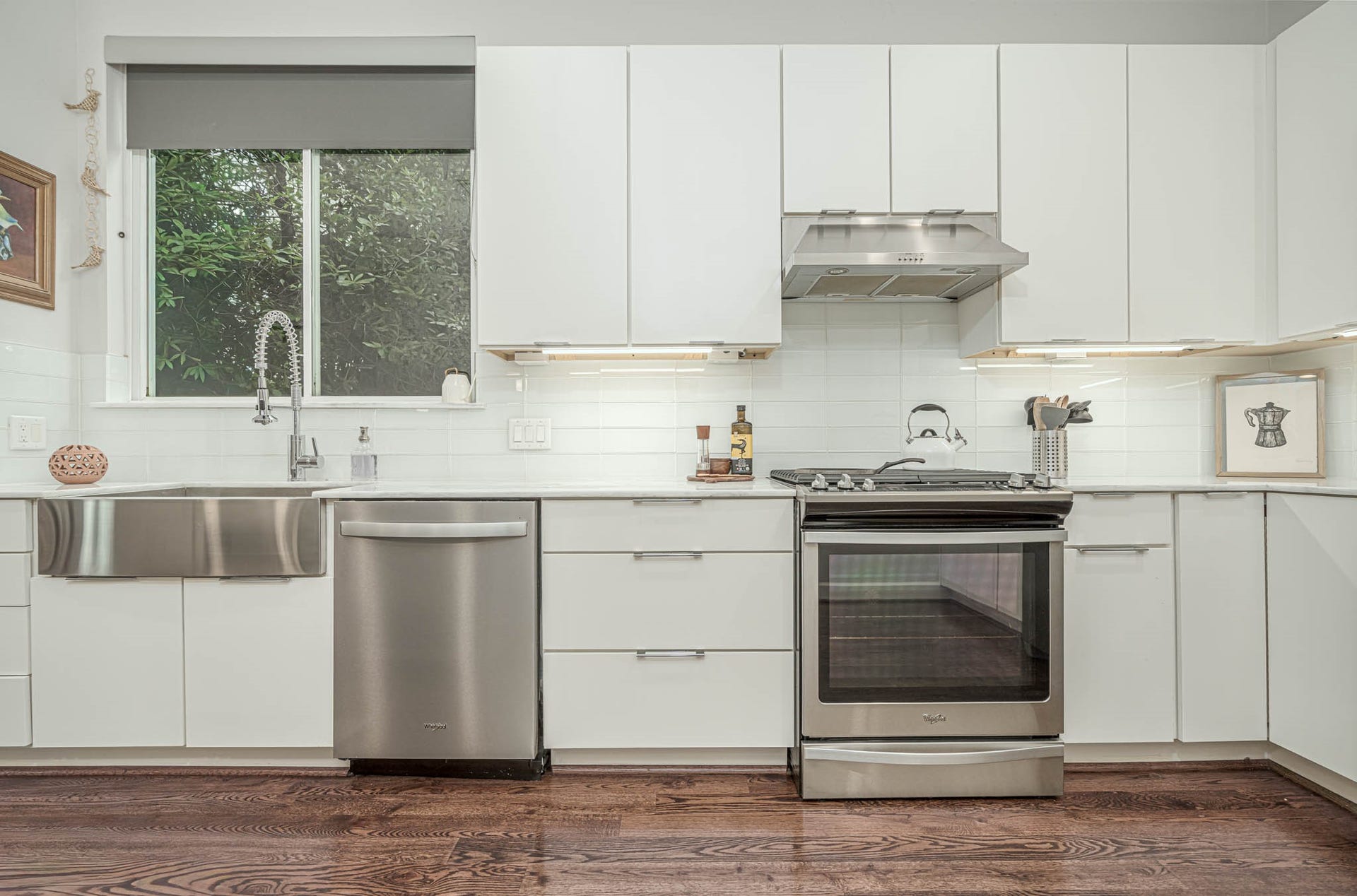 1615 Bingham Street, Houston, TX 77007 Modern kitchen featuring sleek white cabinetry, stainless steel appliances, and a stylish farmhouse sink, complemented by warm hardwood floors.