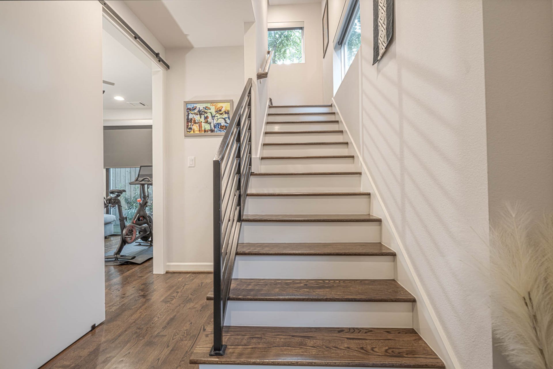 1615 Bingham Street, Houston, TX 77007 Modern staircase with sleek metal railings and wooden steps leading to a bright upper level, adjacent to a versatile room perfect for a home gym.