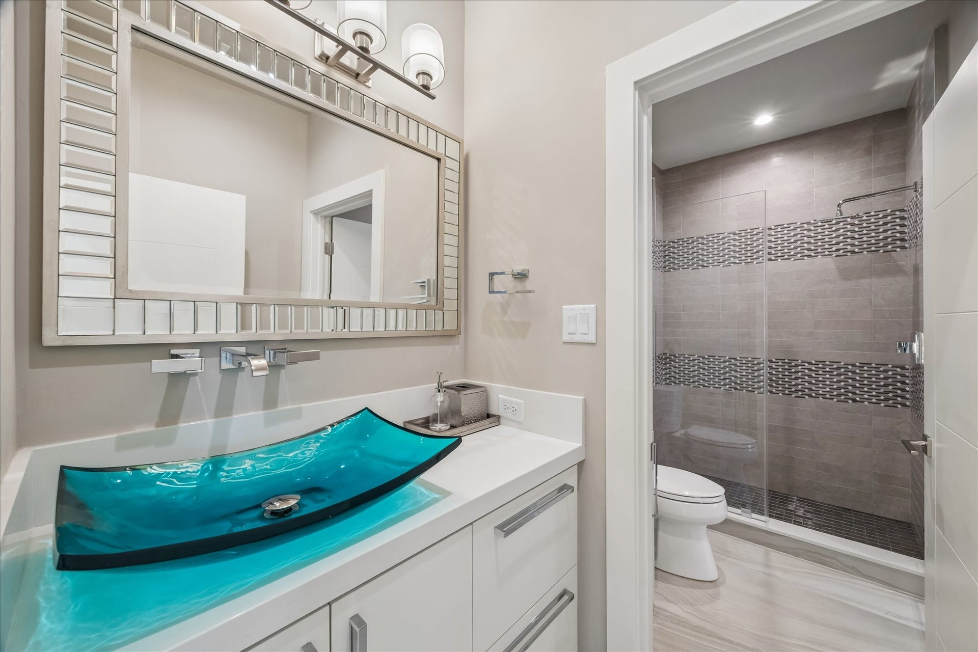 1 Water Key, Hitchcock, TX 77563 The guest bathroom showcases a clean, modern color palette with a double vanity setupone dedicated to the guest bedroom for privacy and an additional vanity accessible from the family room. Features include a turquoise glass vessel sink, quartz countertop, under-vanity lighting, and a spacious walk-in shower