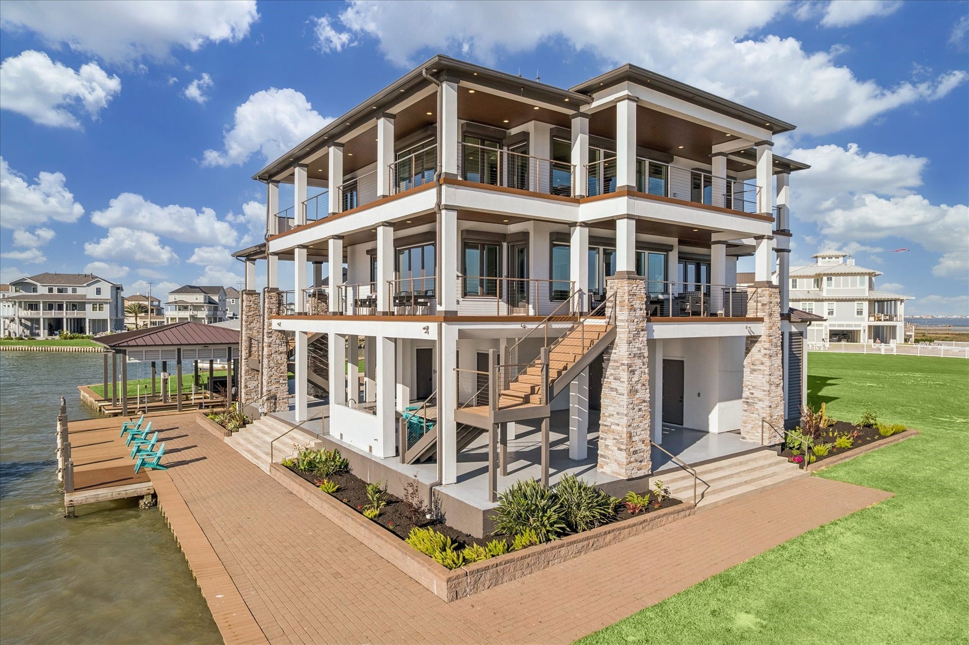 1 Water Key, Hitchcock, TX 77563 A premier outdoor retreat, featuring expansive paver pathways and manicured landscaping that frame a large shaded dockside patio. Above, multi-level covered balconies accented by stone columns and sleek cable railings offer architectural elegance and panoramic views. The seamless flow from the outdoor spaces creates the ultimate waterfront setting for entertaining