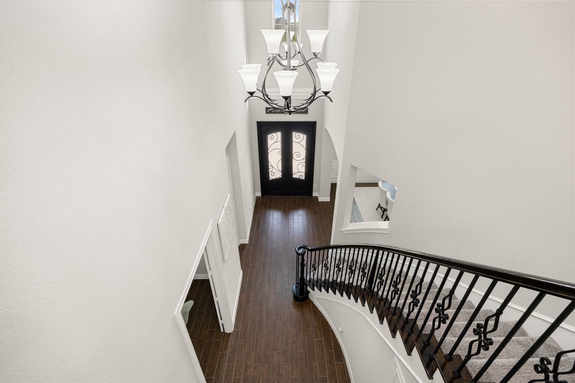 A dramatic two-story entry is framed by an iron chandelier and a curved staircase with wrought iron railing.