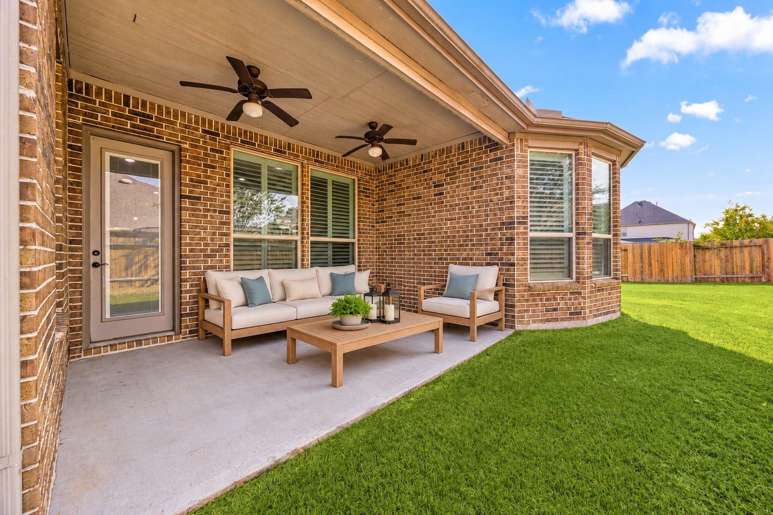The covered back patio features two ceiling fans and brick detailing, offering a comfortable spot to relax or entertain outdoors. Virtually staged.