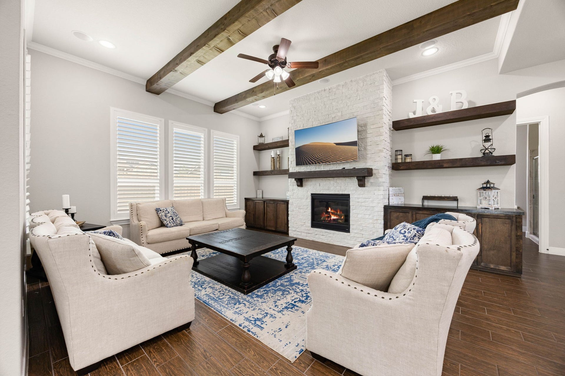 Wood beam ceiling details, a stone fireplace and custom floating shelves bring warmth and character to the main living space.