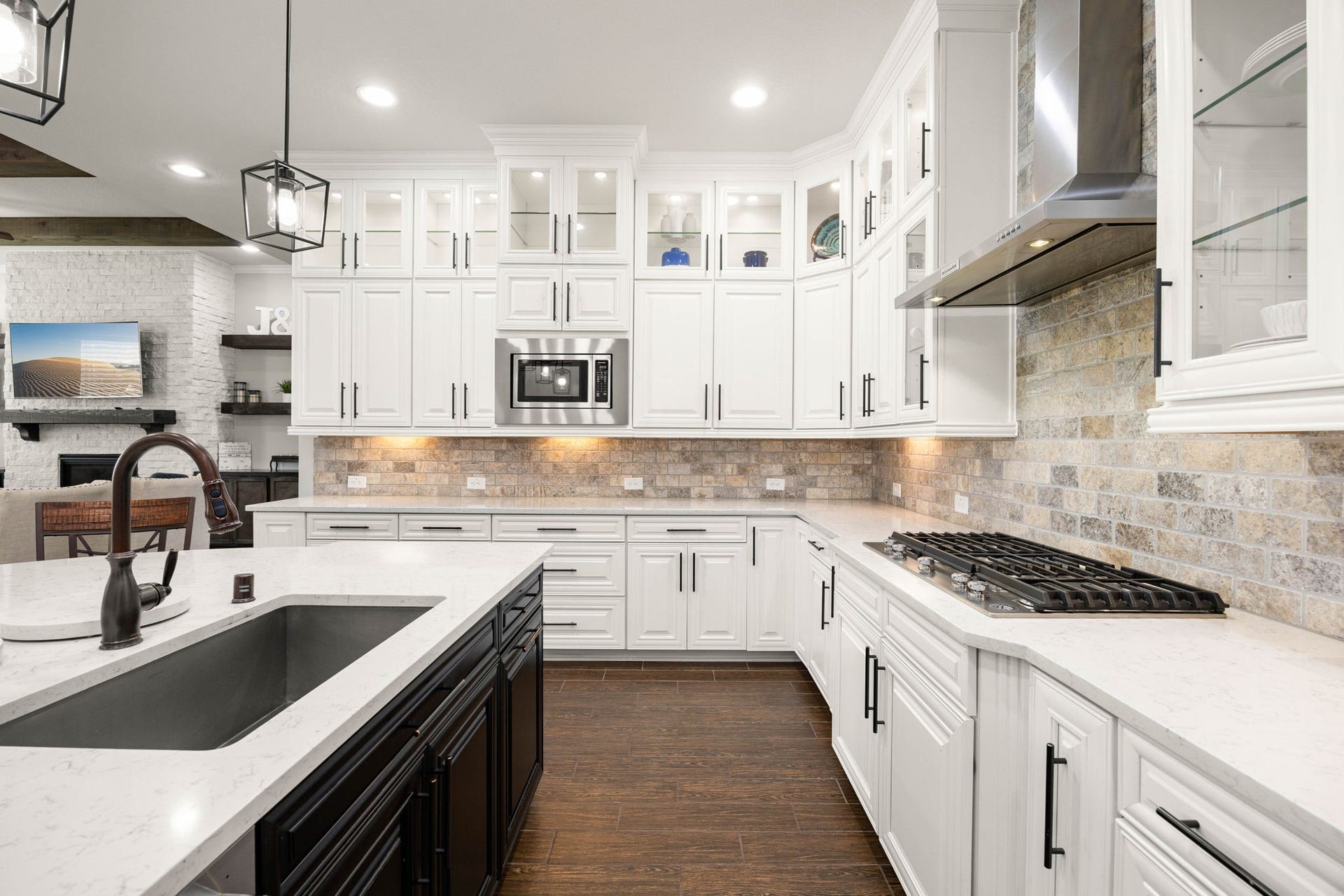 A built-in microwave and gas cooktop are framed by crisp white cabinetry and a stacked stone backsplash that adds texture and warmth throughout the space.