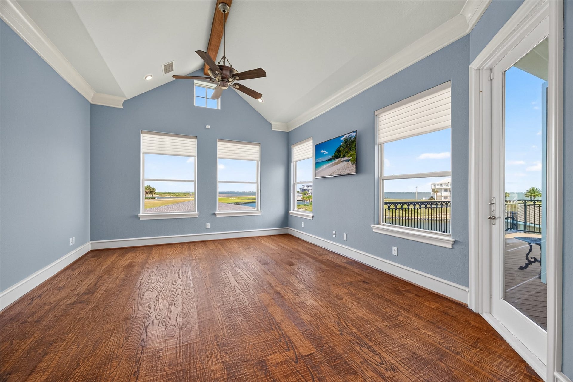 13 Sugarloaf, Hitchcock, TX 77563 Spacious room with hardwood floors and light blue walls, featuring large windows offering stunning water views and abundant natural light, complemented by a stylish ceiling fan and access to a balcony.