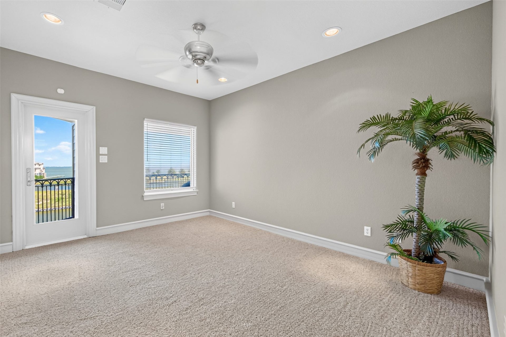 13 Sugarloaf, Hitchcock, TX 77563 Bright, spacious room with a ceiling fan, plush carpeting, and a large window showcasing stunning outdoor views, alongside a door leading to a balcony.