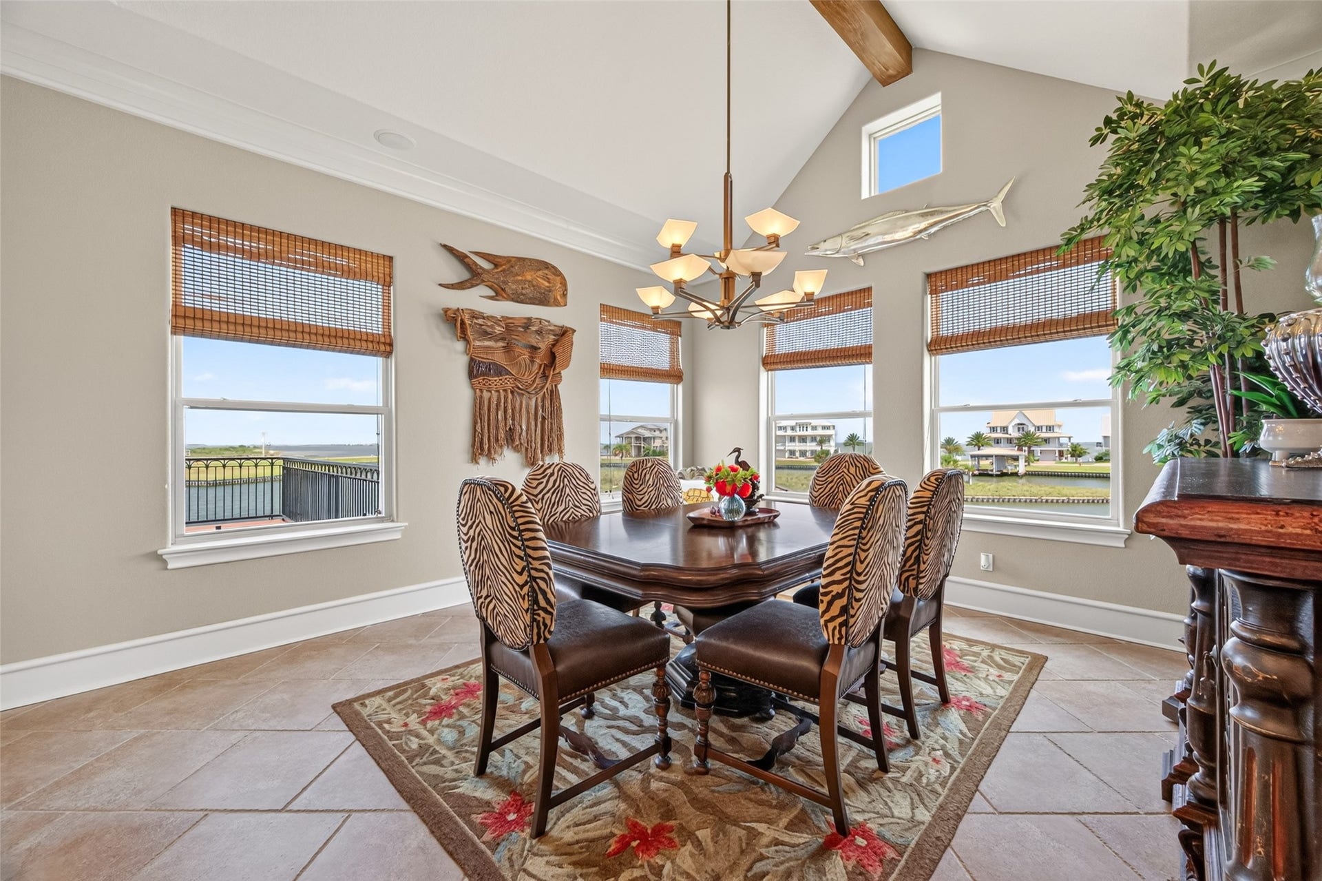 13 Sugarloaf, Hitchcock, TX 77563 Elegant dining room with high ceilings, natural light, and a chic chandelier. Features stylish zebra-patterned chairs, decorative wall art, and expansive windows offering scenic water views.