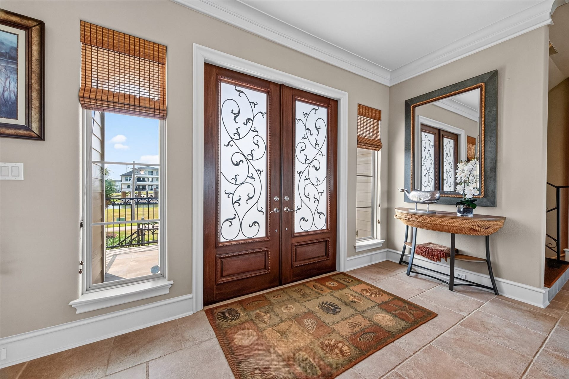 13 Sugarloaf, Hitchcock, TX 77563 Elegant entryway featuring ornate double doors with decorative glass panels. Natural light streams through adjacent windows, highlighting a stylish console table and a large mirror, creating a welcoming and sophisticated atmosphere.