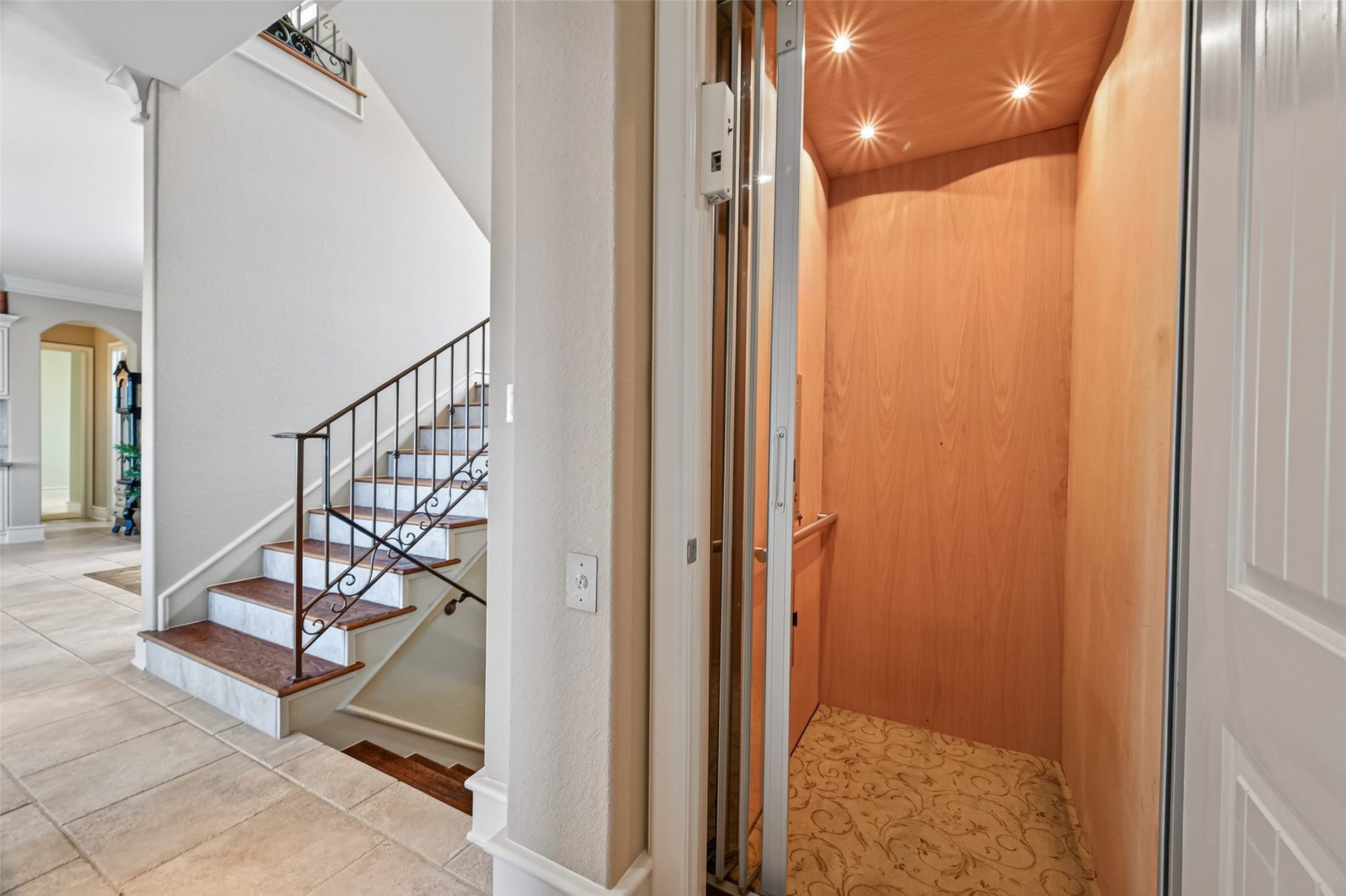 13 Sugarloaf, Hitchcock, TX 77563 Elegant home featuring a convenient in-house elevator next to a stylish staircase with wrought iron railing, set against a backdrop of light tile flooring and open archways.