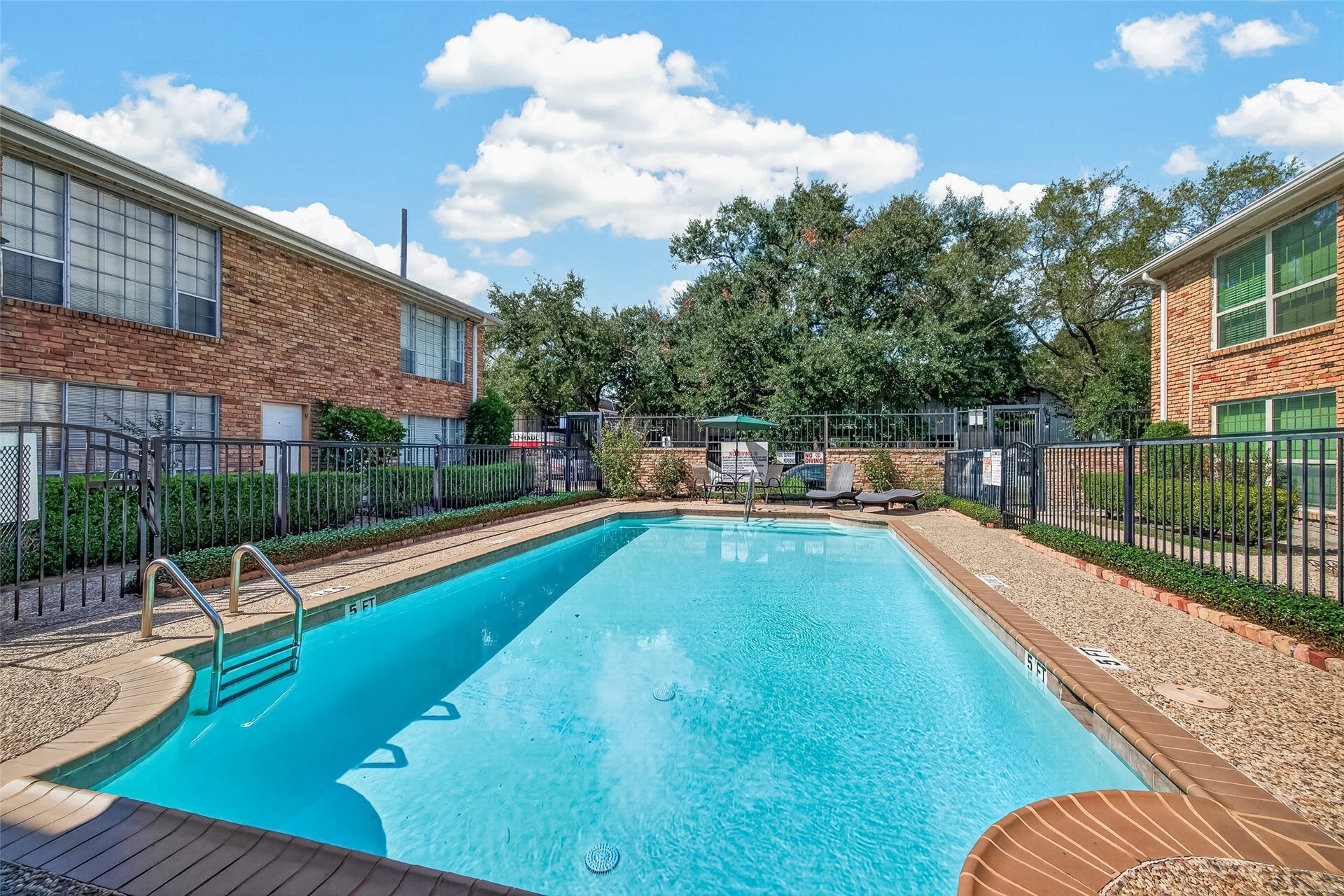 5353 Richmond Avenue, #12, Houston, TX 77056 Dive into relaxation with this inviting community pool, surrounded by lush greenery and charming brick buildings, perfect for unwinding on sunny days.