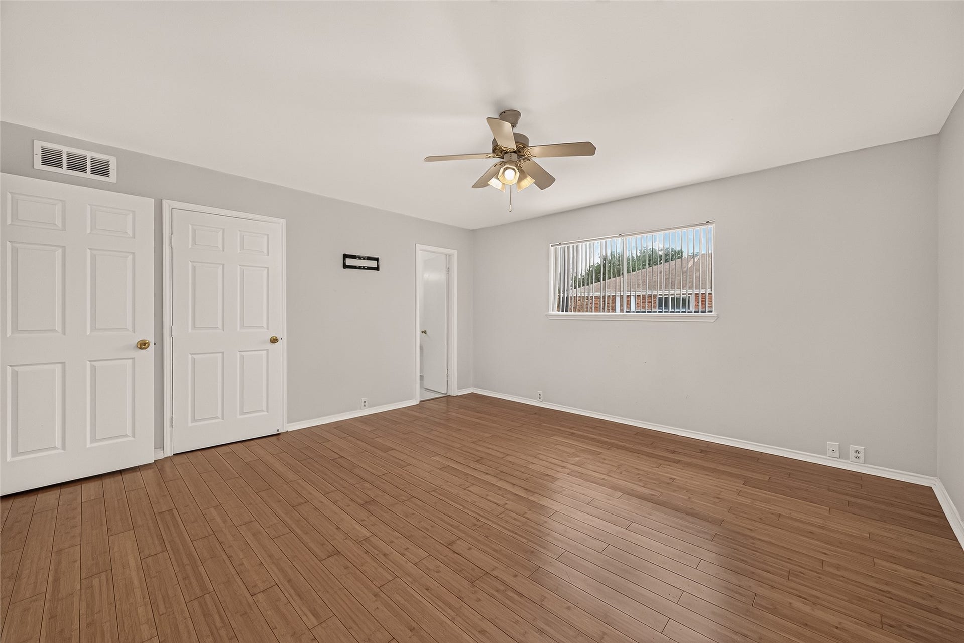 5353 Richmond Avenue, #12, Houston, TX 77056 Spacious bedroom with warm wood-style flooring, neutral walls, and ample natural light from the large window, featuring a ceiling fan and dual closets for convenience.