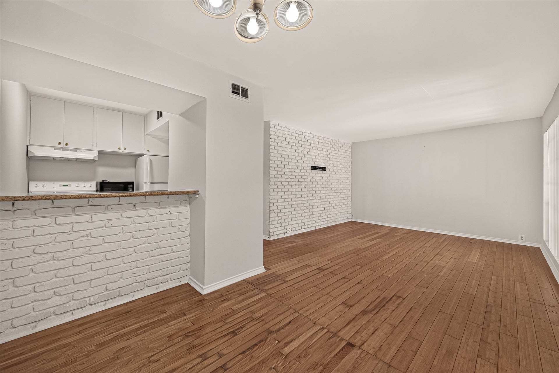5353 Richmond Avenue, #12, Houston, TX 77056 Bright and spacious living area with stylish white brick accents, hardwood floors, and an open kitchen featuring modern appliances and a convenient breakfast bar.