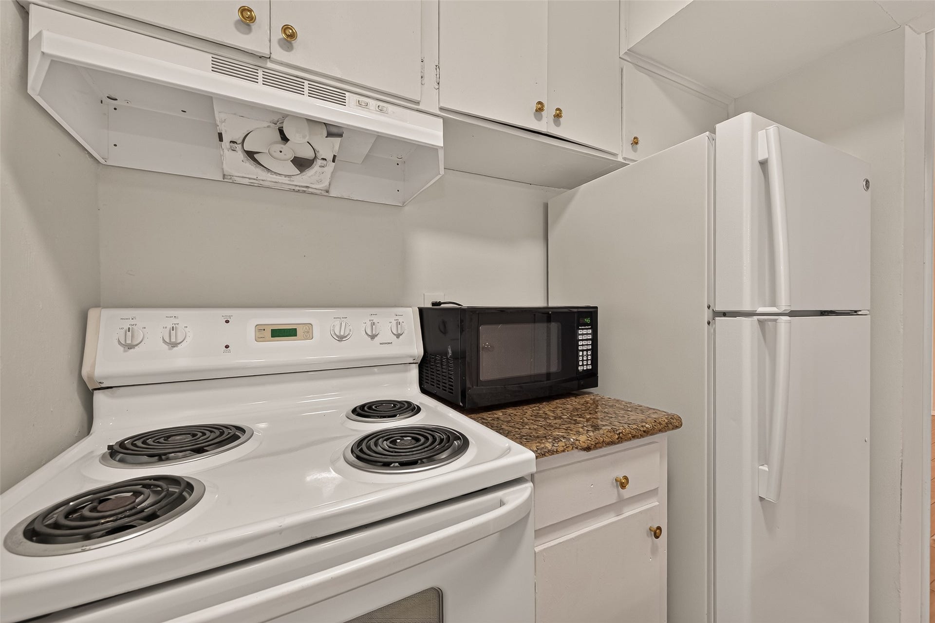 5353 Richmond Avenue, #12, Houston, TX 77056 Compact kitchen with a cozy layout, featuring a white electric stove, a sleek microwave on granite countertops, and ample cabinet storage, ideal for efficient cooking.