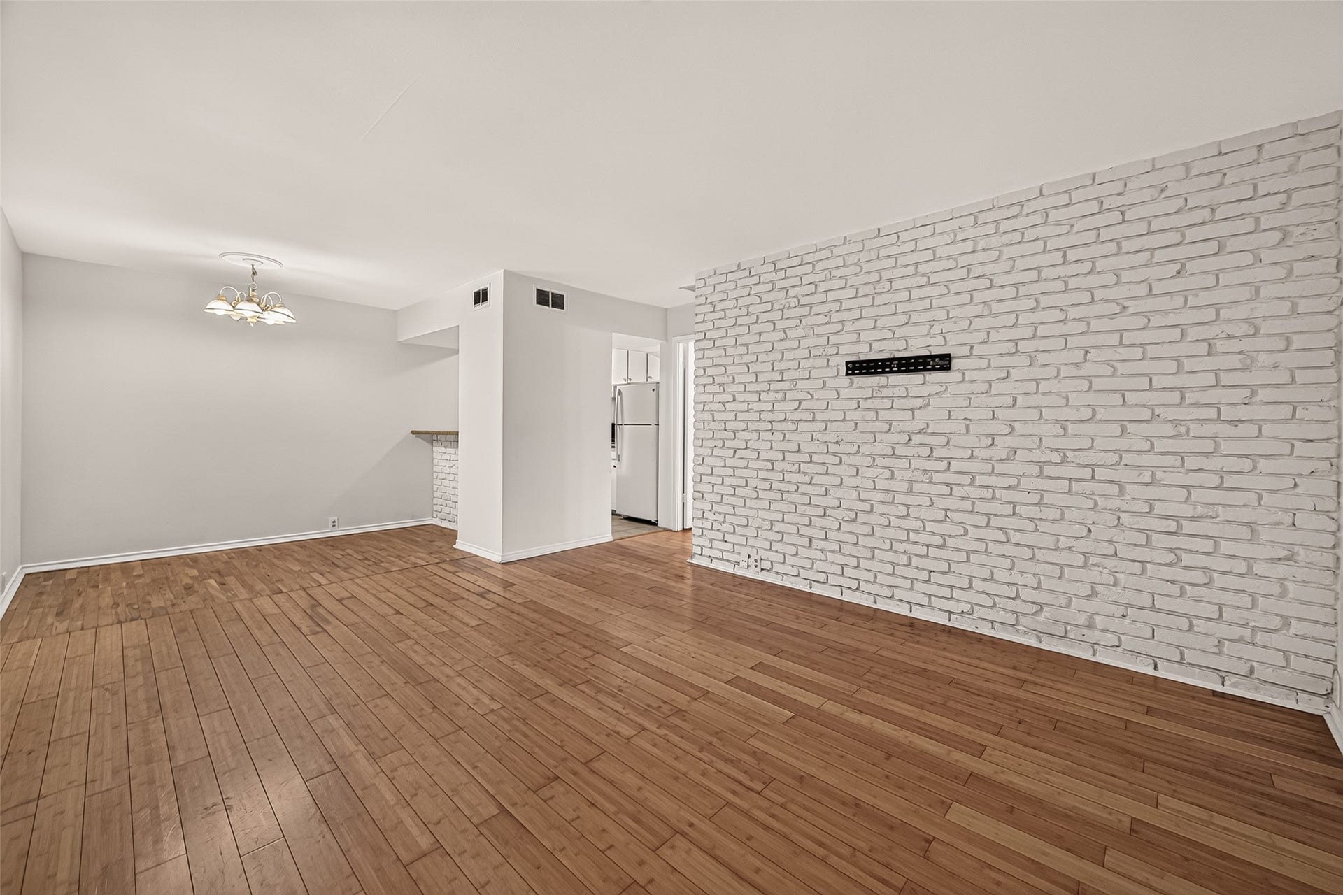 5353 Richmond Avenue, #12, Houston, TX 77056 Spacious living area with elegant hardwood floors and a striking white brick accent wall, offering a modern and inviting atmosphere.