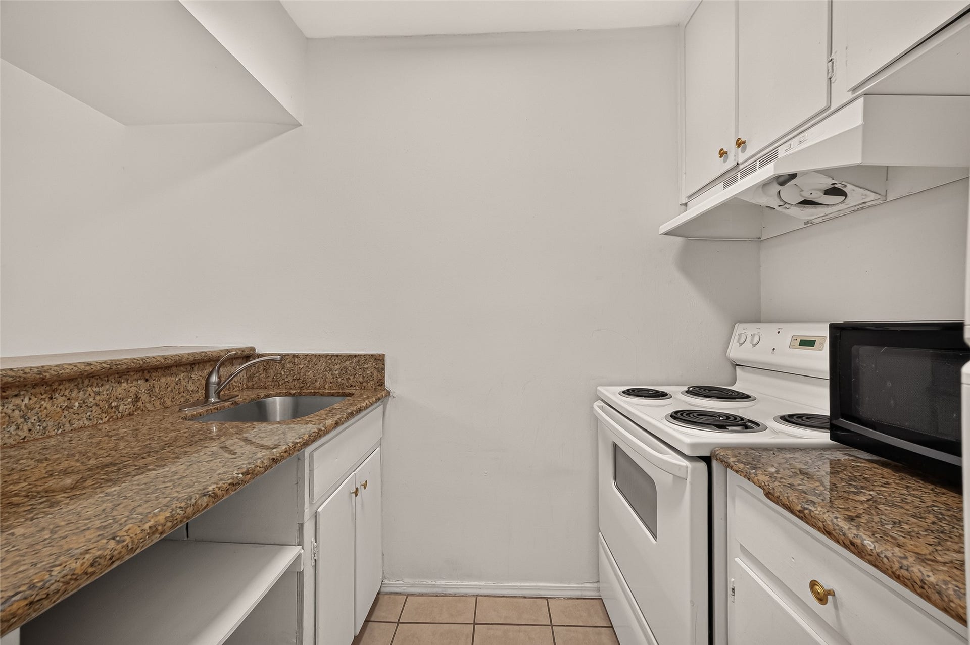 5353 Richmond Avenue, #12, Houston, TX 77056 Compact kitchen with elegant granite countertops, white cabinetry, and a modern electric stove, offering efficiency and style.