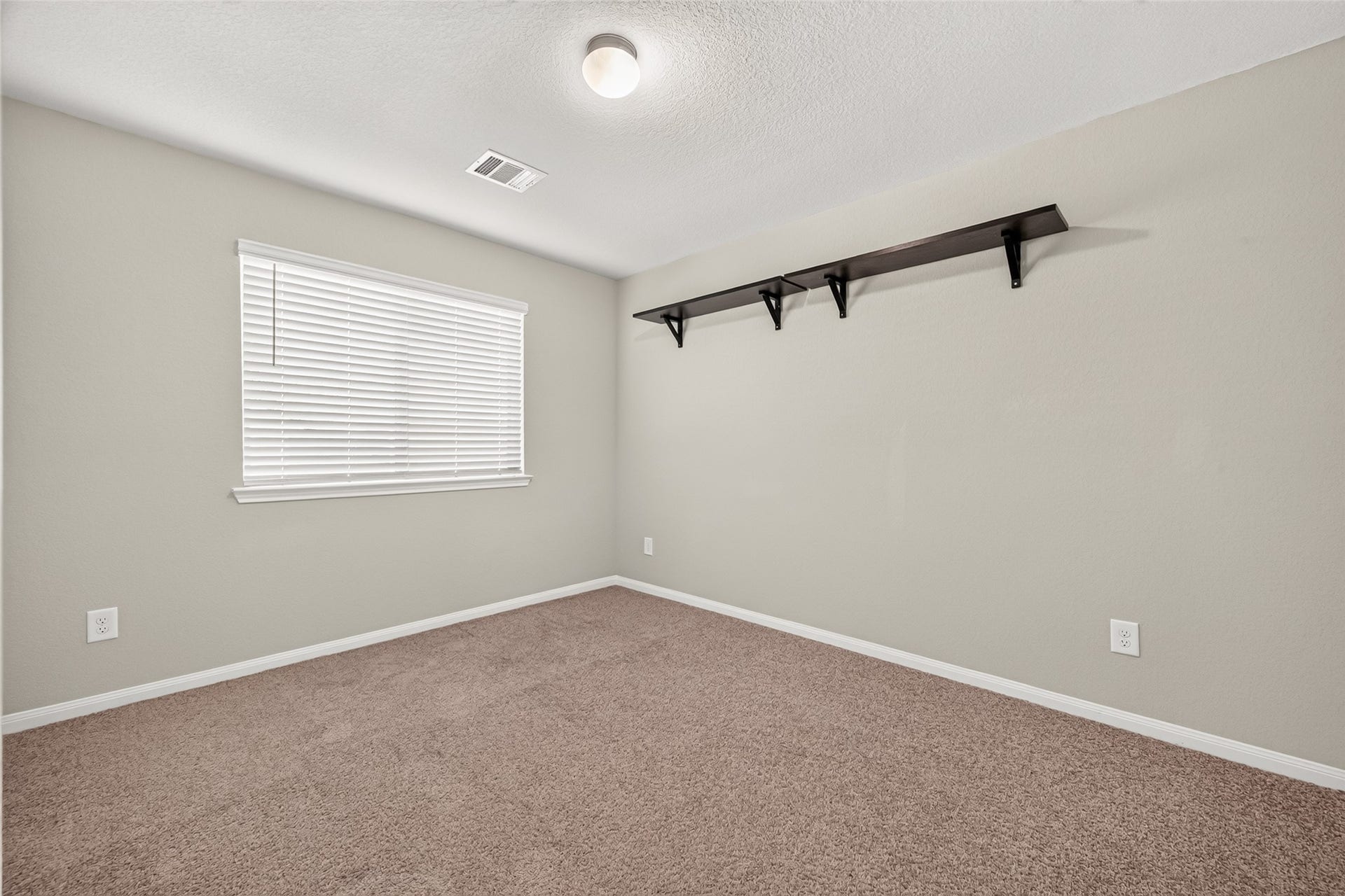 13405 Cannon Creek Court, Willis, TX 77378 Bedroom 3 with plush carpeting, soft neutral walls, and ample natural light from a large window, featuring a sleek wall-mounted shelf for added storage.