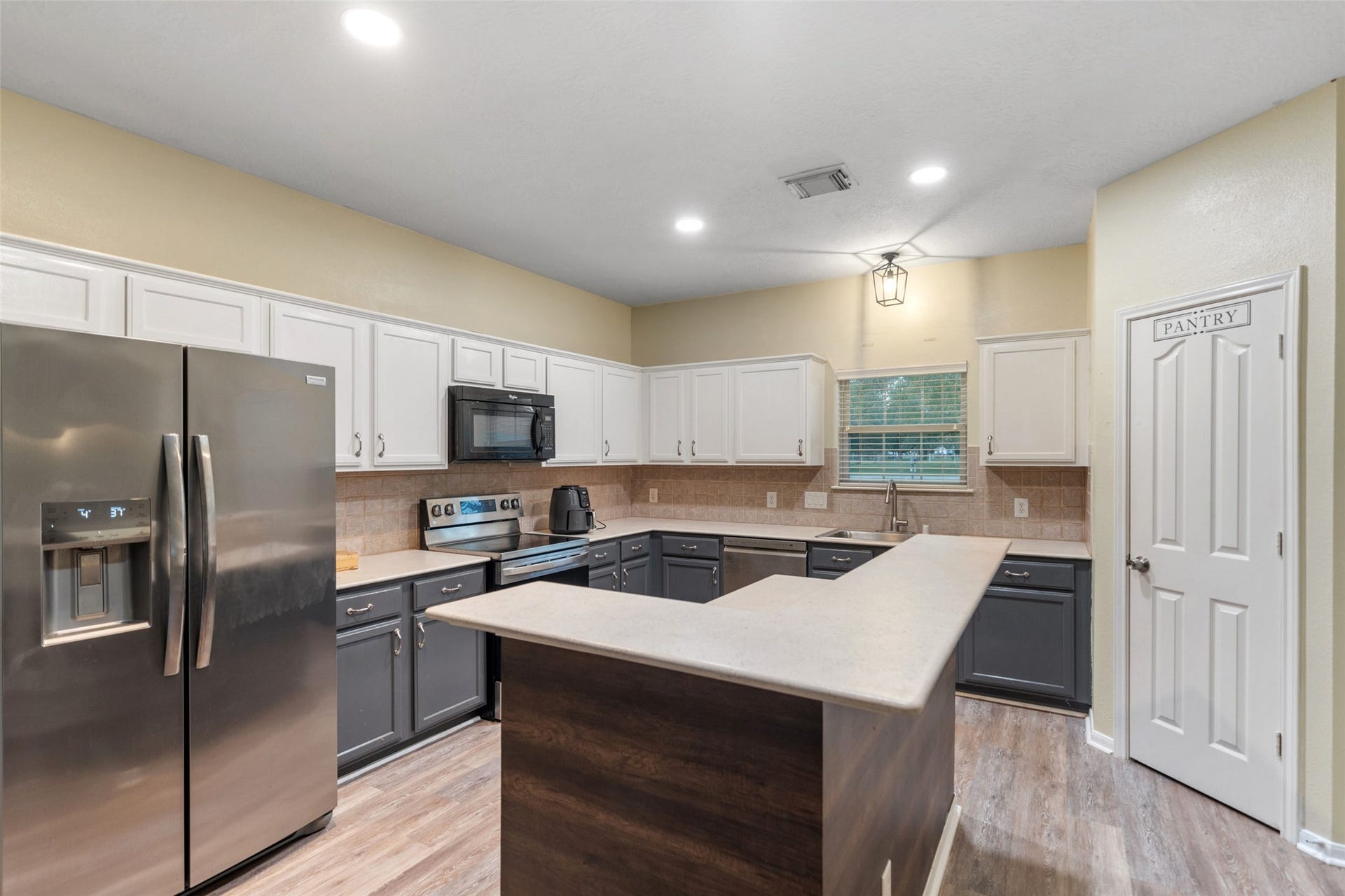Functional kitchen with ample cabinetry, stainless steel dishwasher, and window over the sink for natural light.