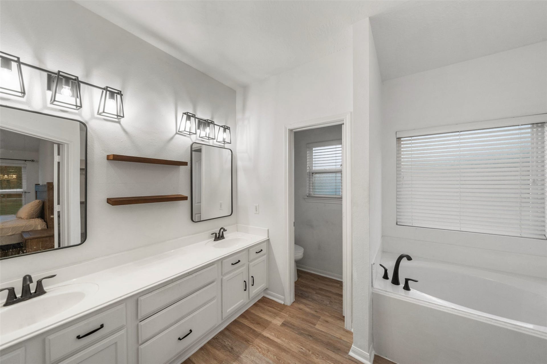 Updated primary bathroom featuring a dual-sink vanity, modern lighting, floating shelves, and ample storage.