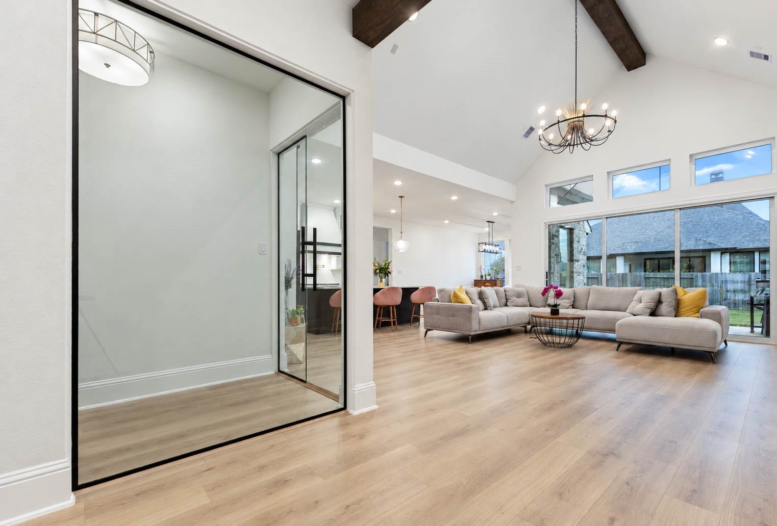 4839 Summer Place Court, Fulshear, TX 77441 Spacious open-concept living area with vaulted ceilings, showcasing a cozy sectional, elegant chandelier, and abundant natural light from sliding doors overlooking the backyard. Pay attention to the glass enclosed bar! Simply Wow.