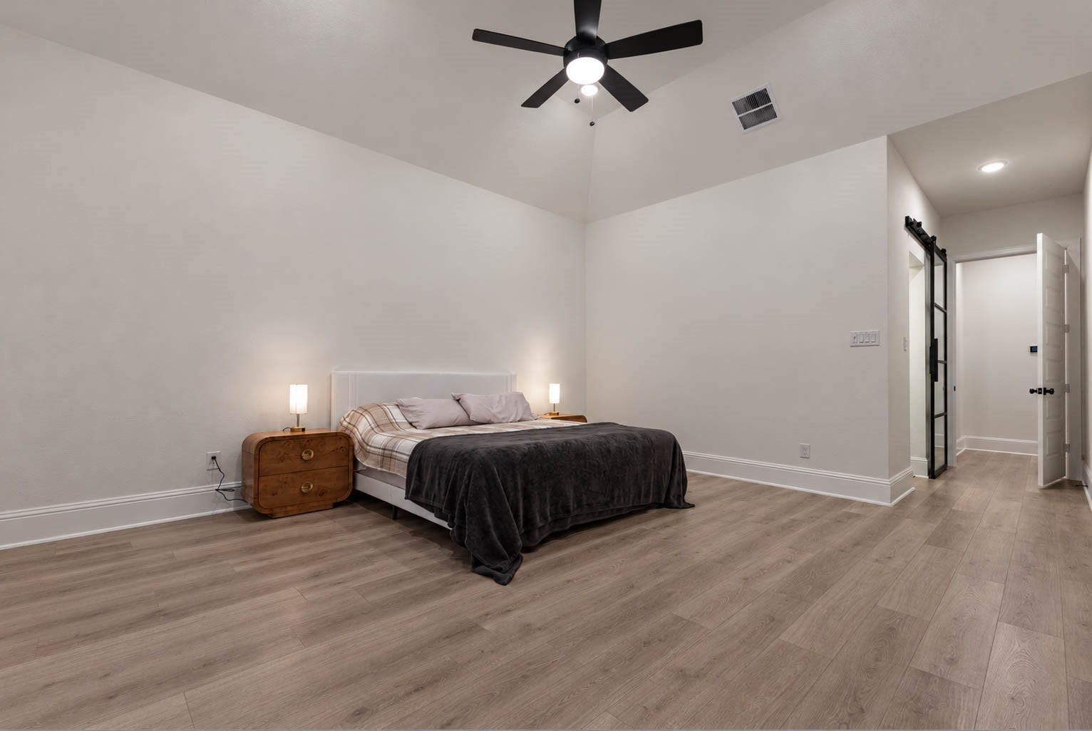 4839 Summer Place Court, Fulshear, TX 77441 Spacious primary bedroom with high ceilings, featuring elegant wood flooring, a modern ceiling fan, and a sleek barn door leading to an en-suite bathroom.