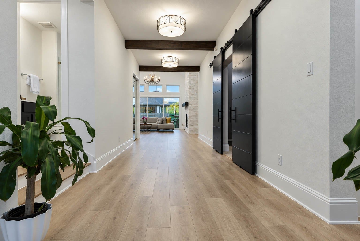 4839 Summer Place Court, Fulshear, TX 77441 Elegant hallway featuring sleek wood flooring and modern light fixtures, leading to a spacious living area with large windows and a cozy fireplace.
