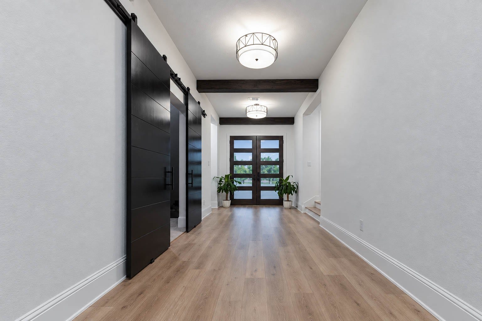 4839 Summer Place Court, Fulshear, TX 77441 Stunning entryway with elegant wood flooring, modern lighting, and sleek black barn doors for the media room, leading to a bright space with large windows and natural light.