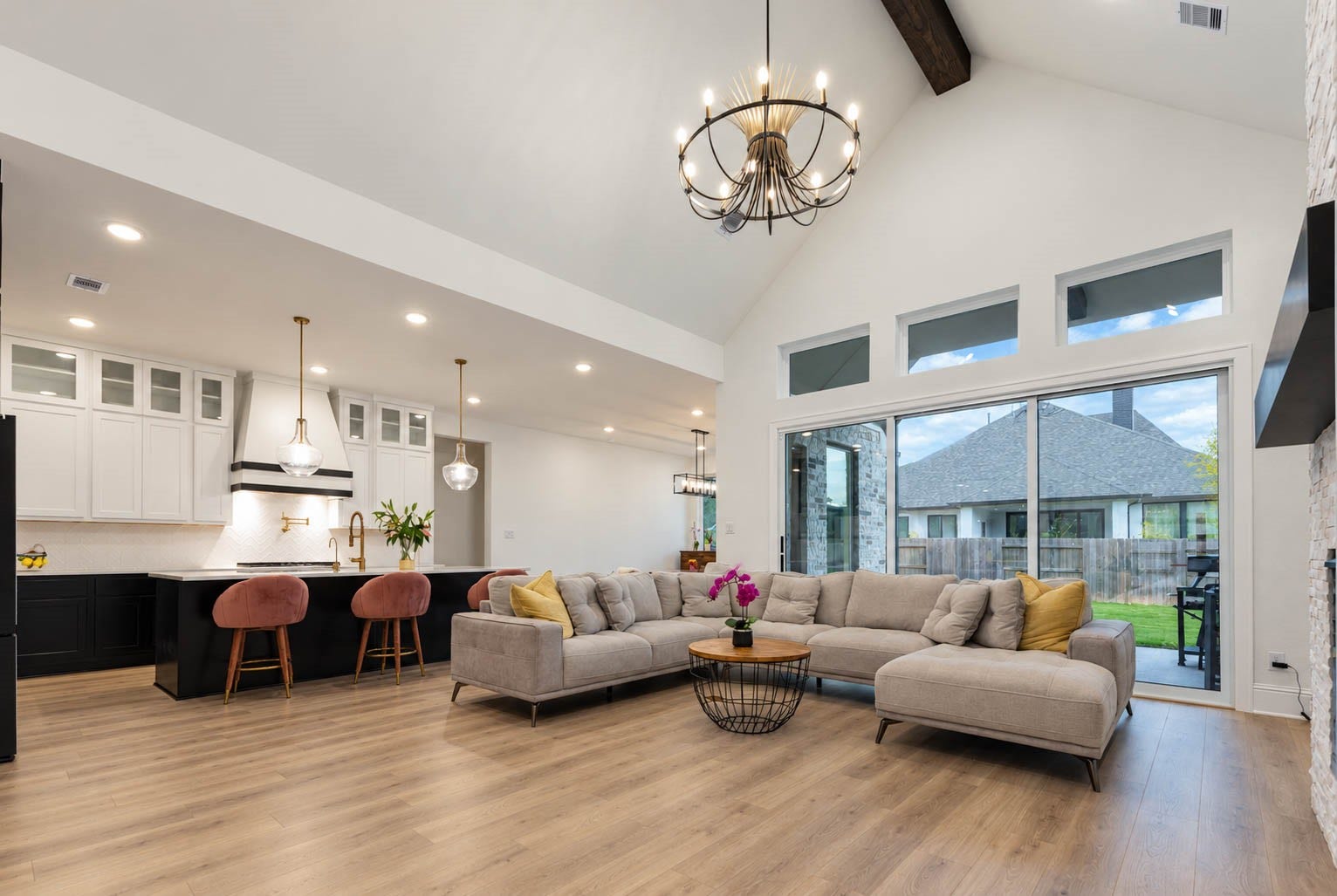 4839 Summer Place Court, Fulshear, TX 77441 Spacious open-concept living area with vaulted ceilings, elegant chandelier, and modern kitchen featuring a stylish island with seating and pendant lights. Expansive windows enhance natural light and offer a view of the backyard. Sliding doors.
