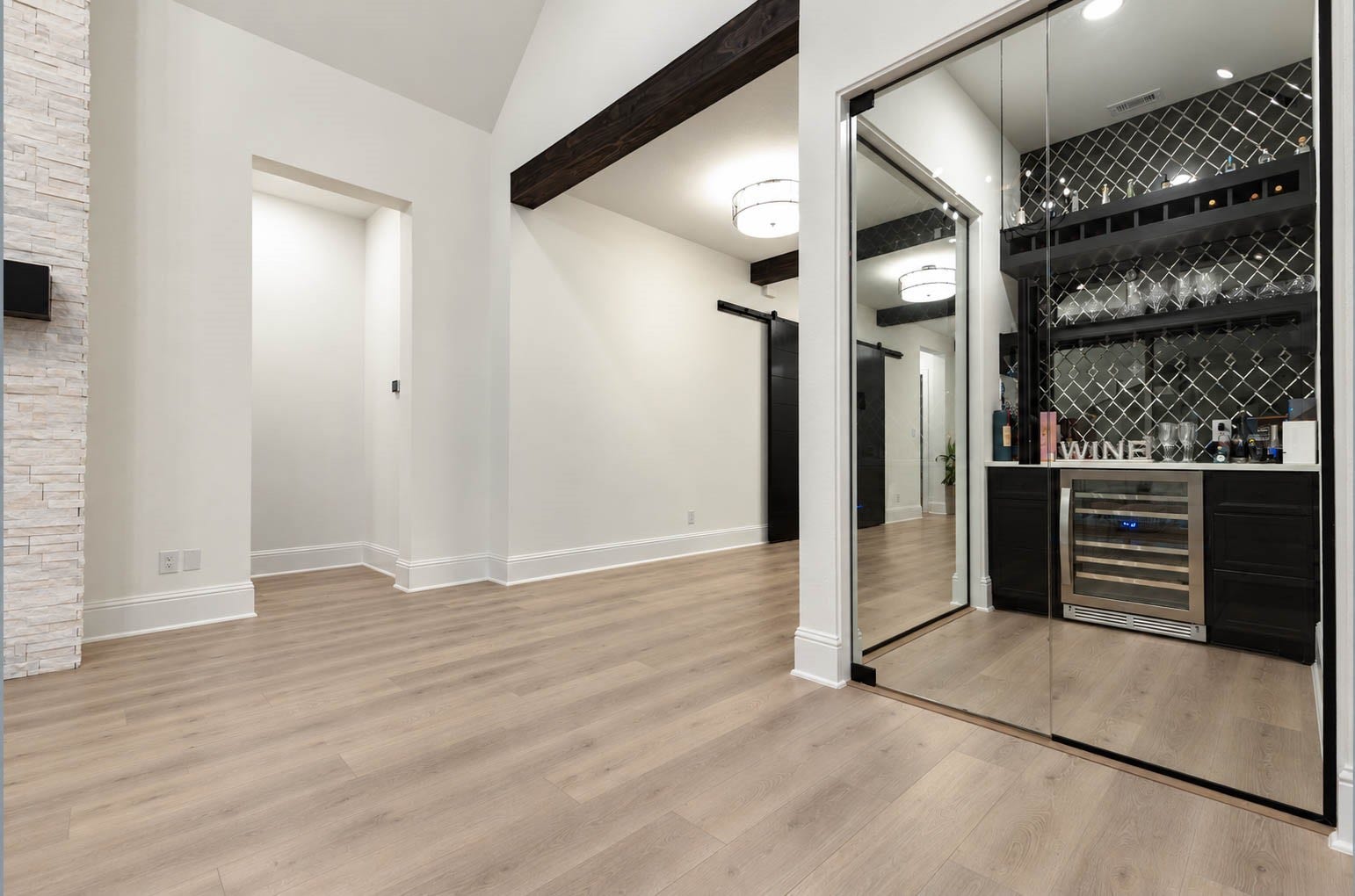 4839 Summer Place Court, Fulshear, TX 77441 Elegant room featuring a sleek wine bar with mirrored sliding doors, chic backsplash, and modern lighting, complemented by warm wood flooring and exposed beams. Cheers!