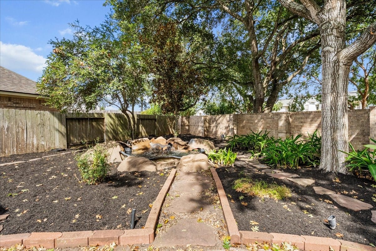 311 Lake Front Drive, League City, TX 77573 Landscaped backyard with stone-edged beds, a pond feature, and big mature trees.
