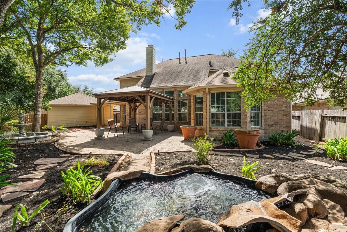311 Lake Front Drive, League City, TX 77573 Private backyard retreat with a serene water feature, oversized pergola, and paver patio under large shade trees.